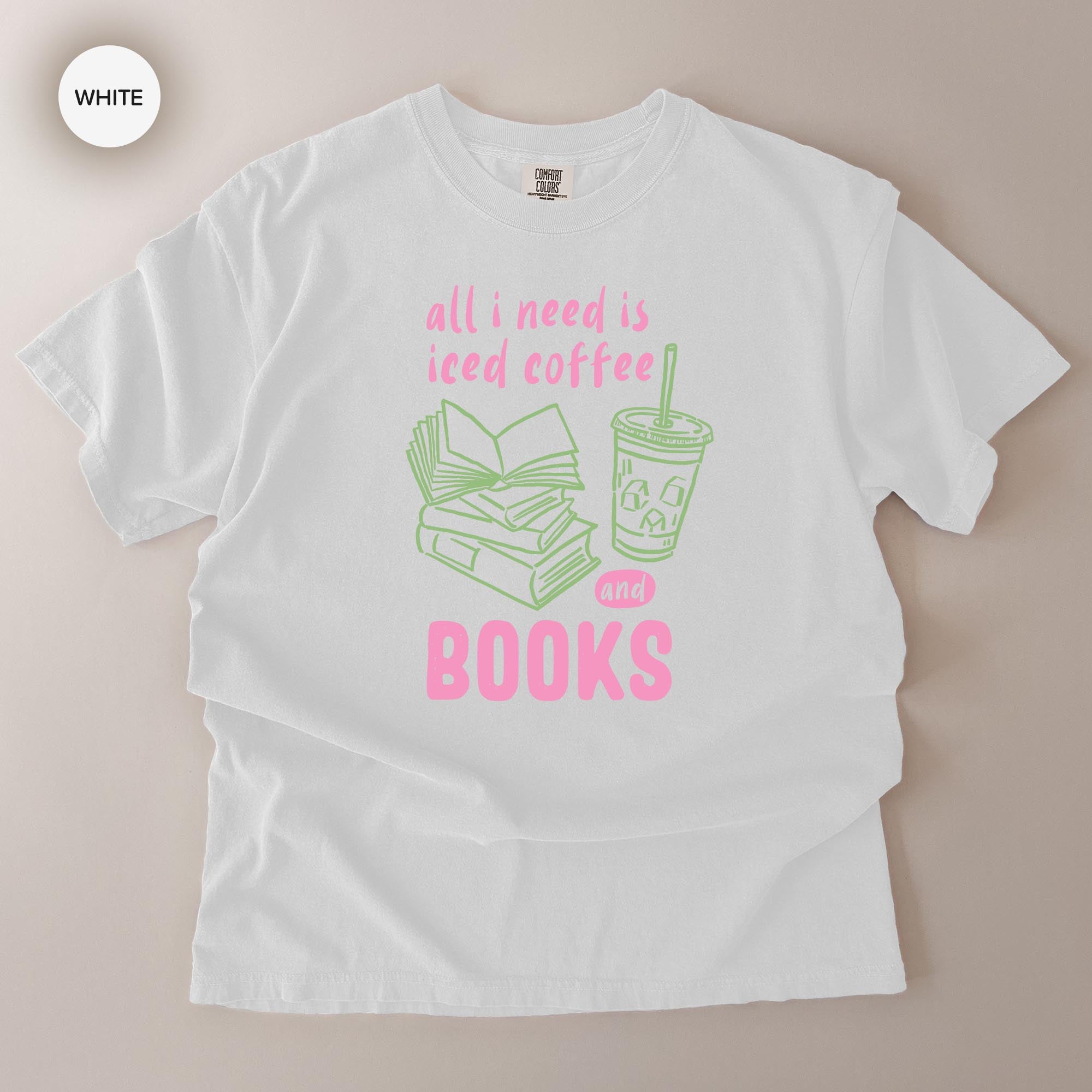 A white t-shirt with a graphic design that says "all I need is iced coffee and books" in pink and green text.