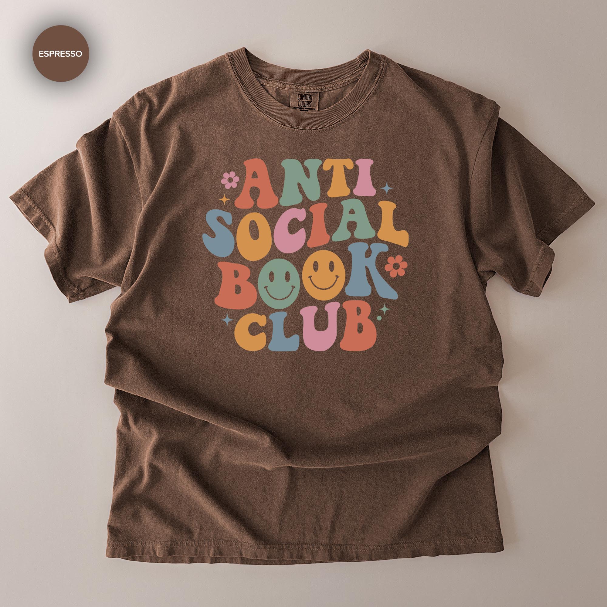 A brown t-shirt with a colorful graphic design that says "ANTI SOCIAL BOOK CLUB" in a playful, retro style.
