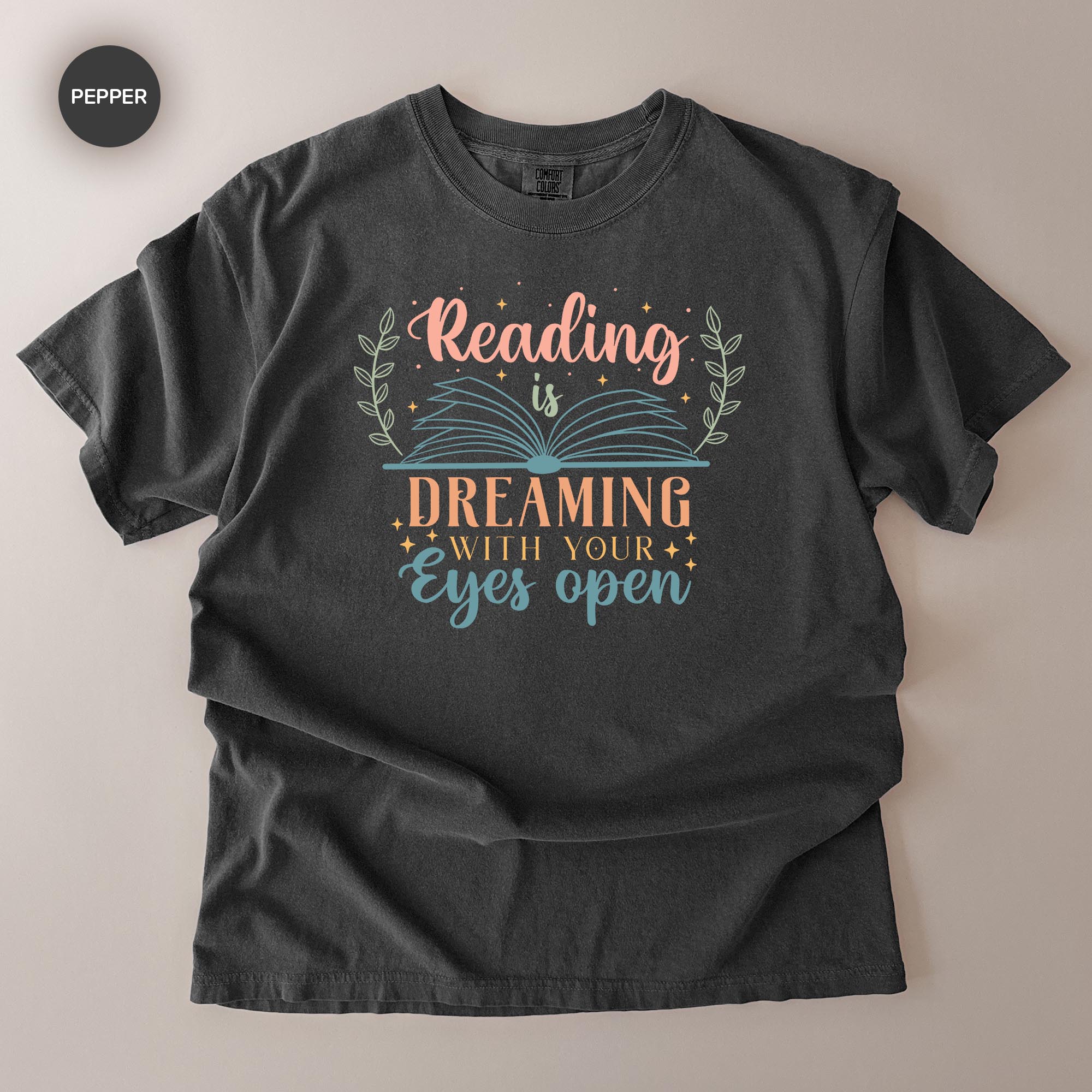 A gray t-shirt with a printed design that says "Reading is Dreaming with your eyes open".