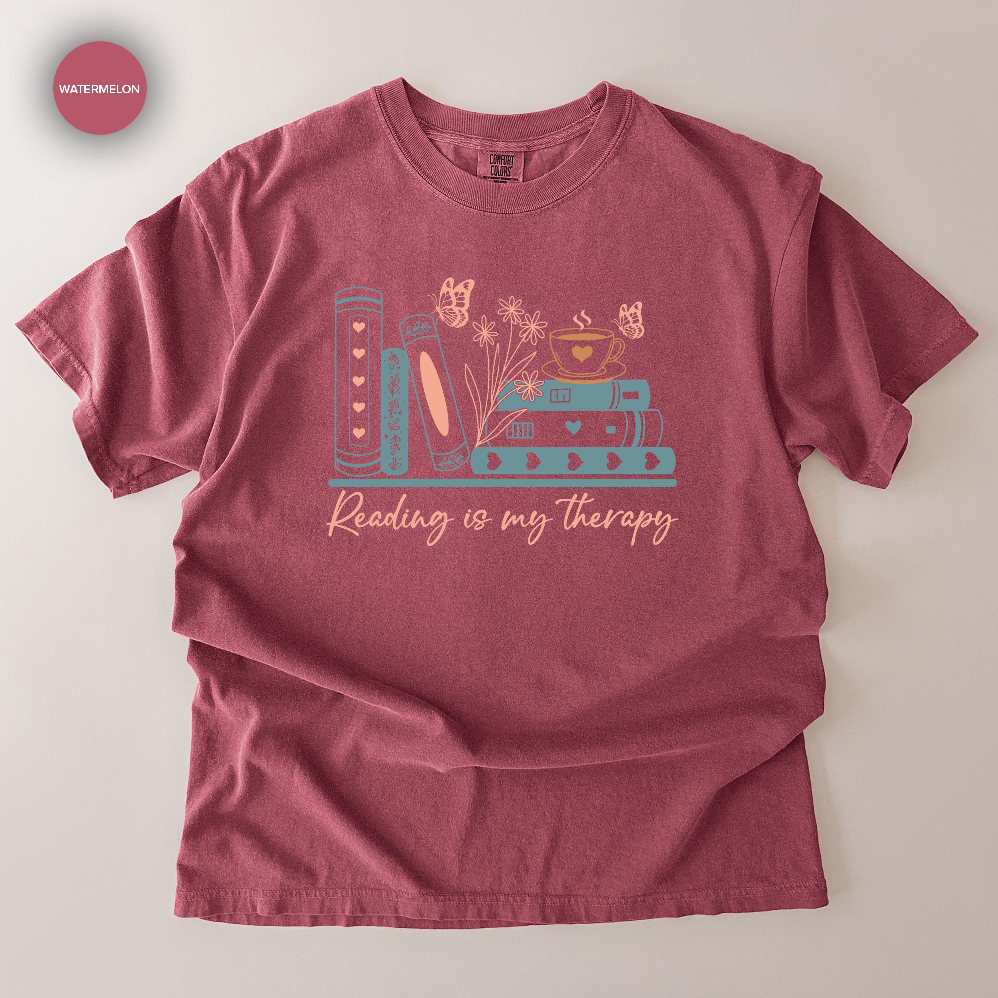 A red t-shirt with a graphic design featuring a stack of books, flowers, and butterflies, along with the text "Reading is my therapy".