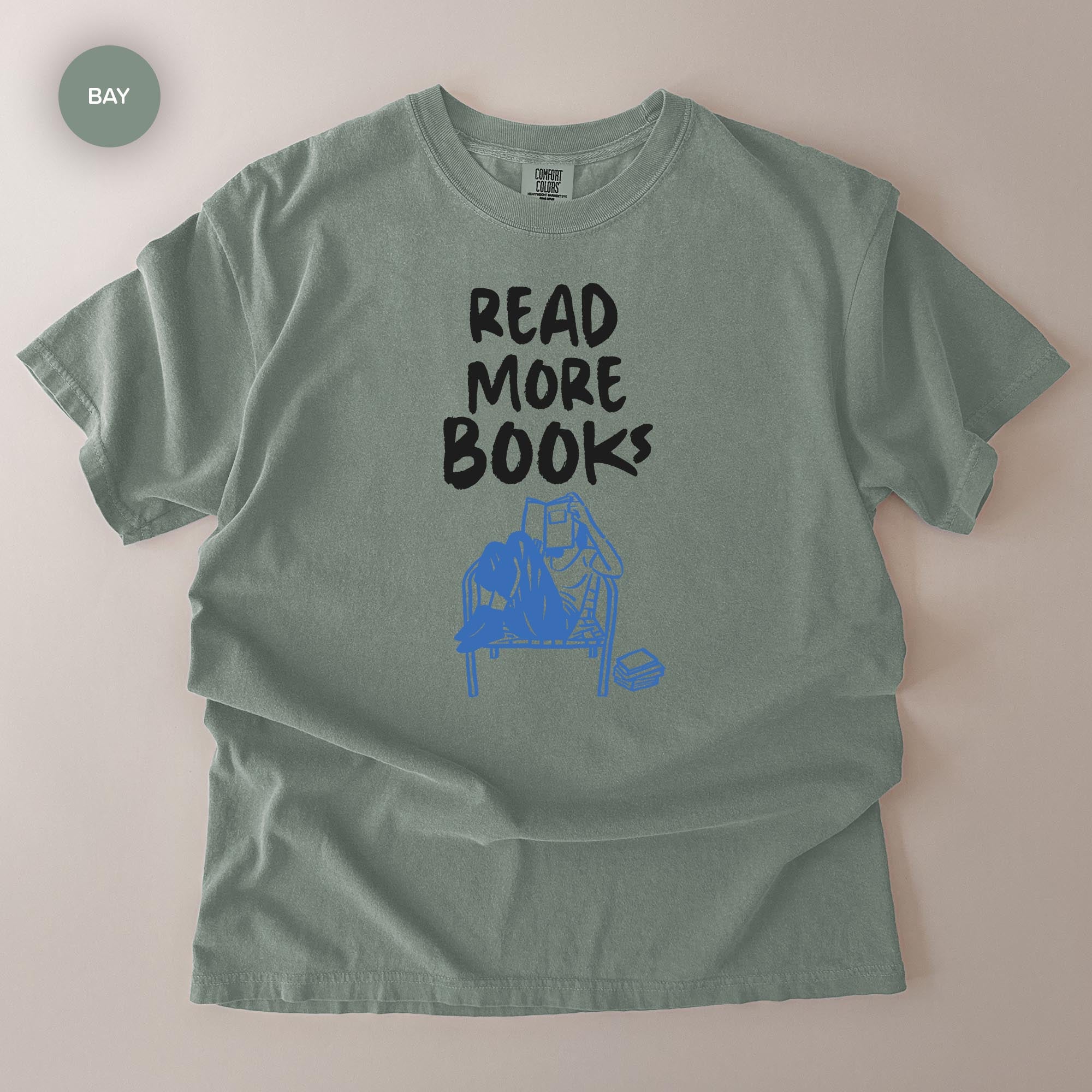 A gray t-shirt with the text "READ MORE BOOKS" printed on it, along with a graphic of a person reading a book.