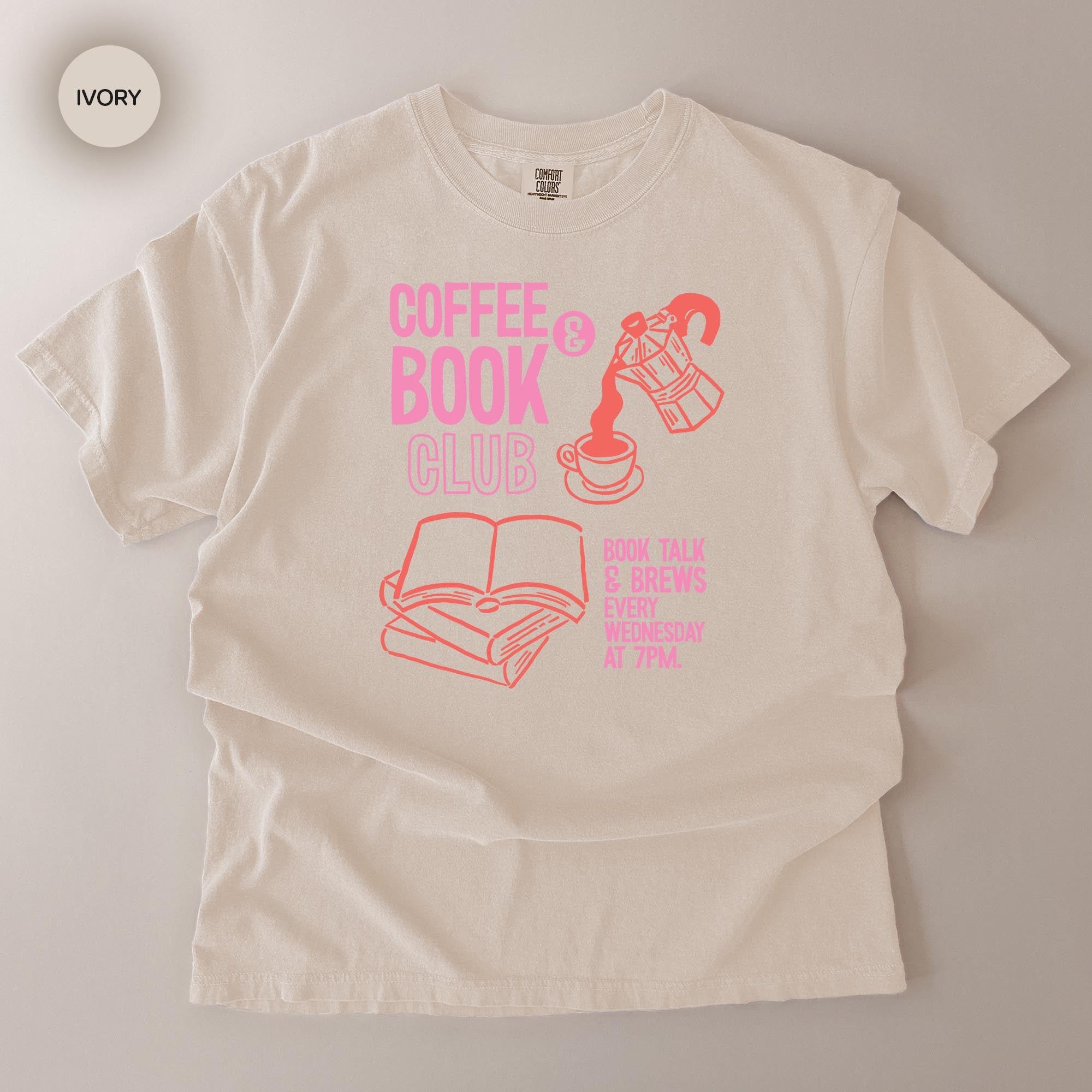 A white t-shirt with a graphic design featuring a coffee cup, an open book, and a teapot, along with text that reads "COFFEE BOOK CLUB" and "SEE TALK ABOUT BOOKS EVERY WEEKEND 7PM".