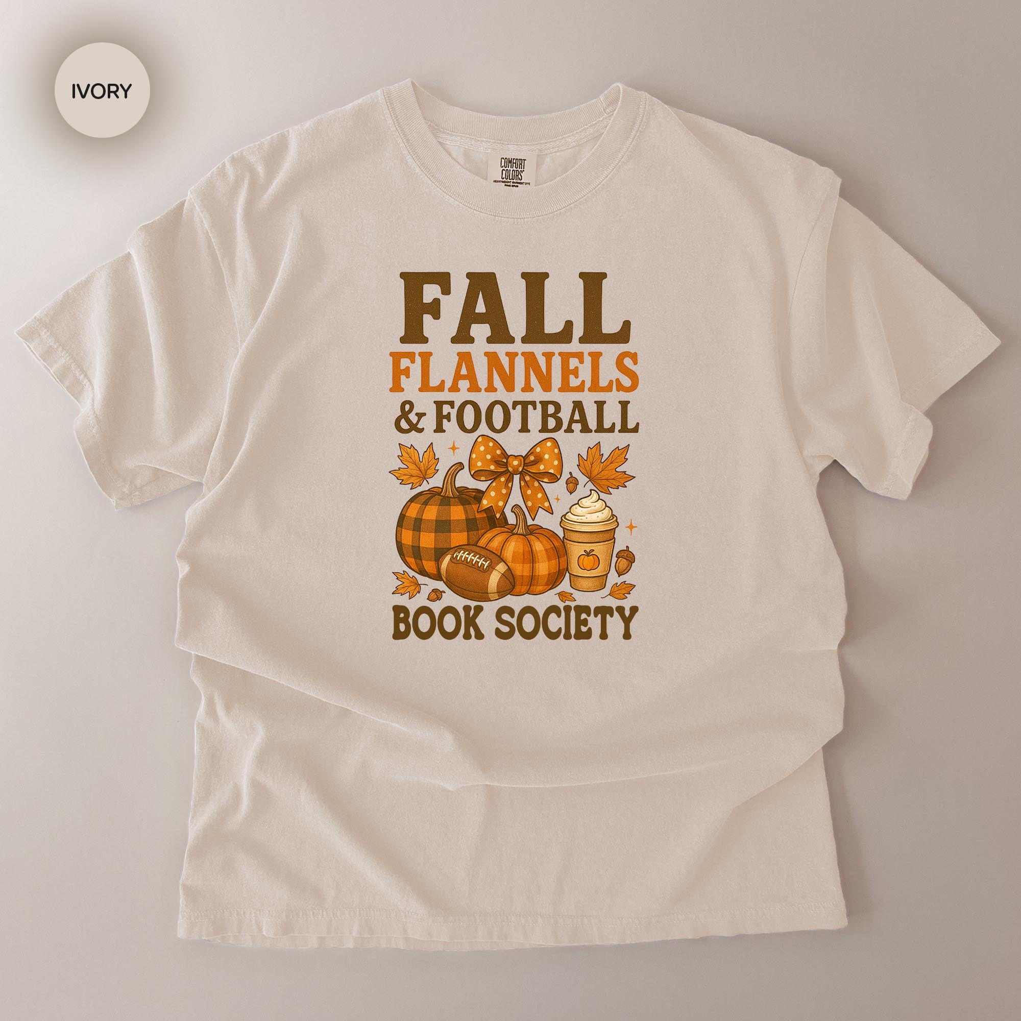 A white t-shirt with a graphic design featuring fall-themed elements such as pumpkins, footballs, and a book, along with the text "FALL FLANNELS & FOOTBALL BOOK SOCIETY".