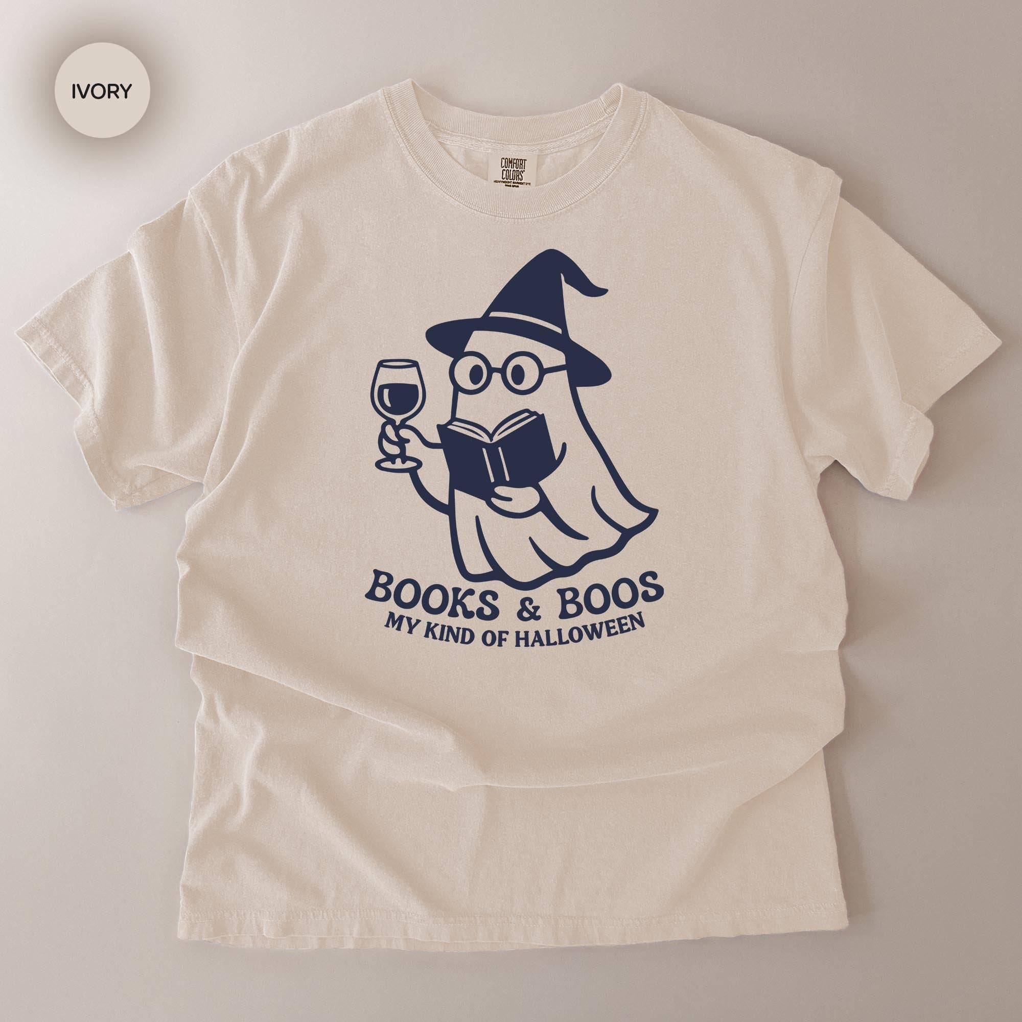 A white t-shirt with a graphic design depicting a ghost character holding a book and a wine glass, along with the text "Books & Boo's MY KIND OF HALLOWEEN".