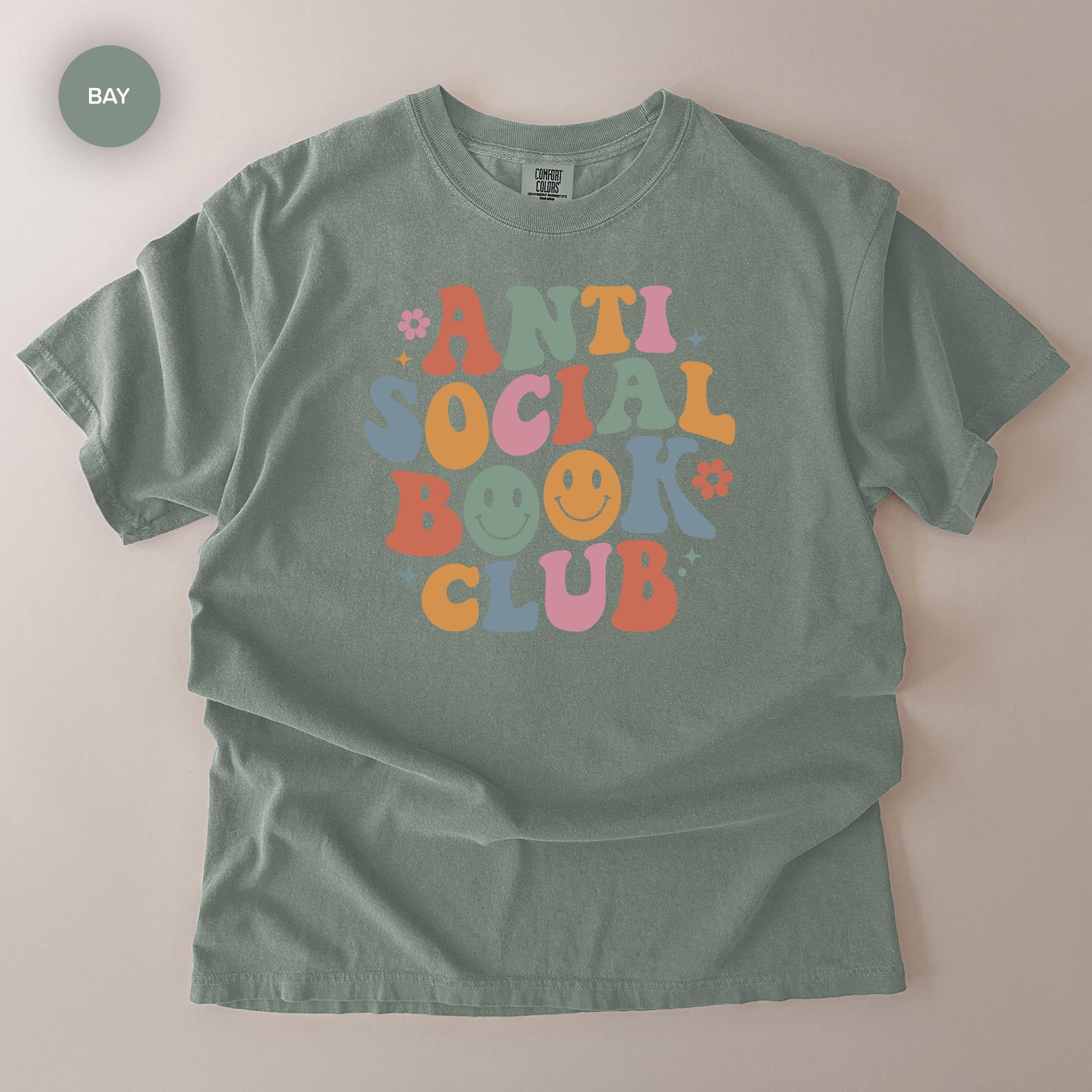 A gray t-shirt with a colorful graphic design that says "ANTI SOCIAL BOOK CLUB" in a playful, retro style.