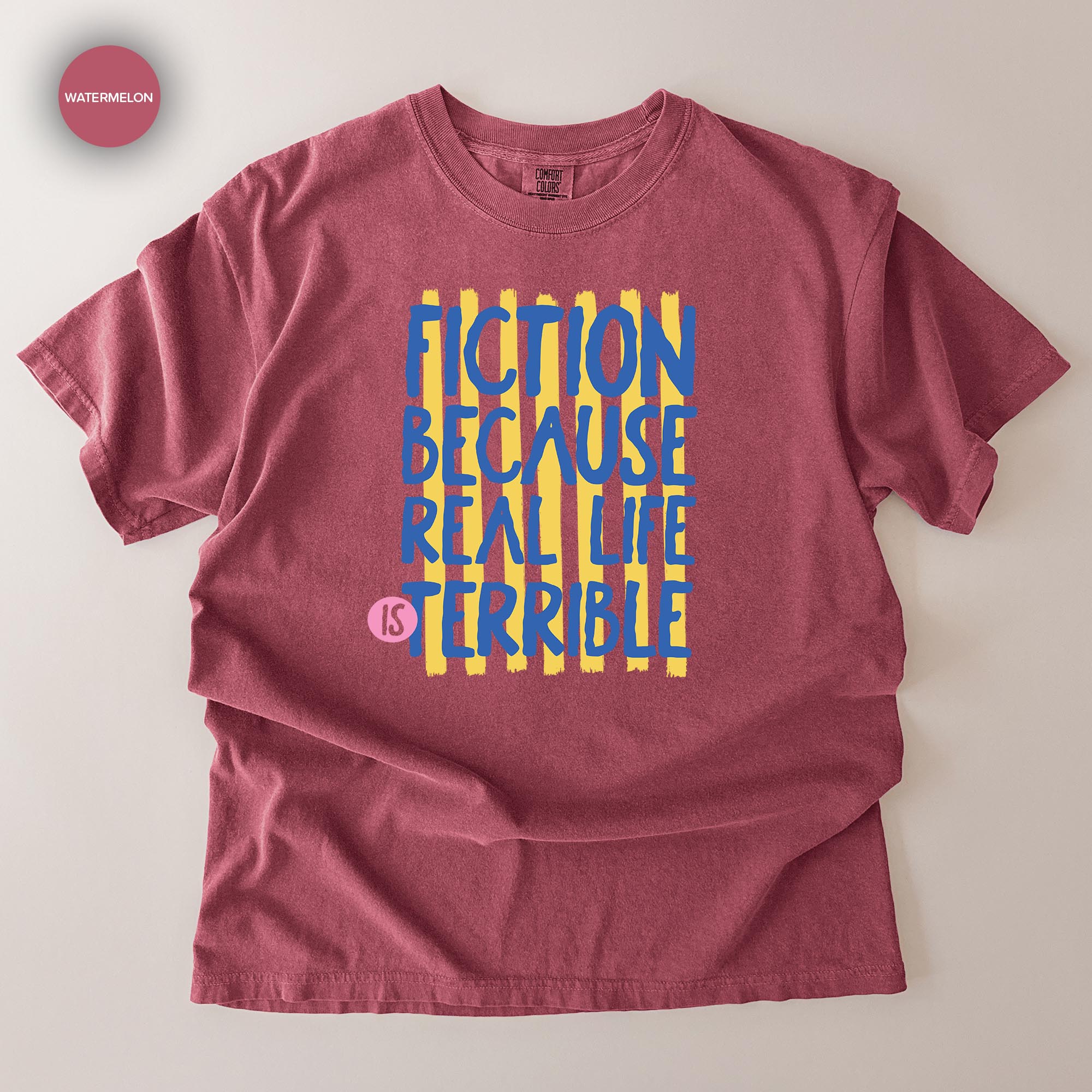A red t-shirt with a graphic design featuring the text "FICTION BECAUSE REAL LIFE IS TERRIBLE" in a bold, stylized font.