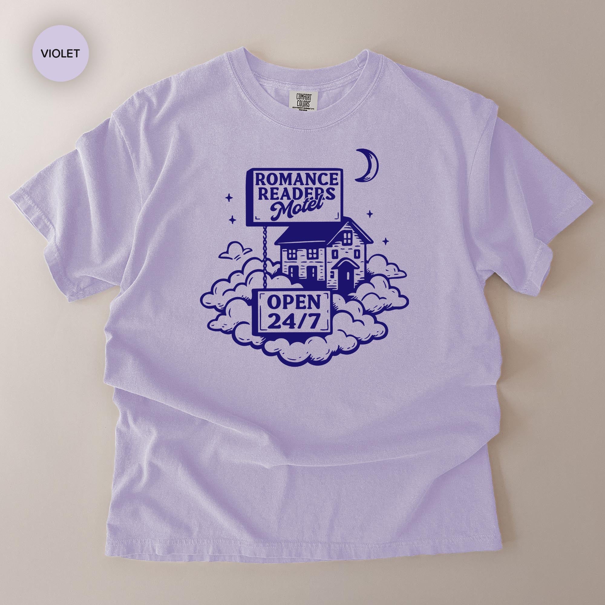 A white t-shirt with a graphic design featuring a house, clouds, and a crescent moon, along with text that reads "ROMANCE READERS MOILET" and "OPEN 24/7".