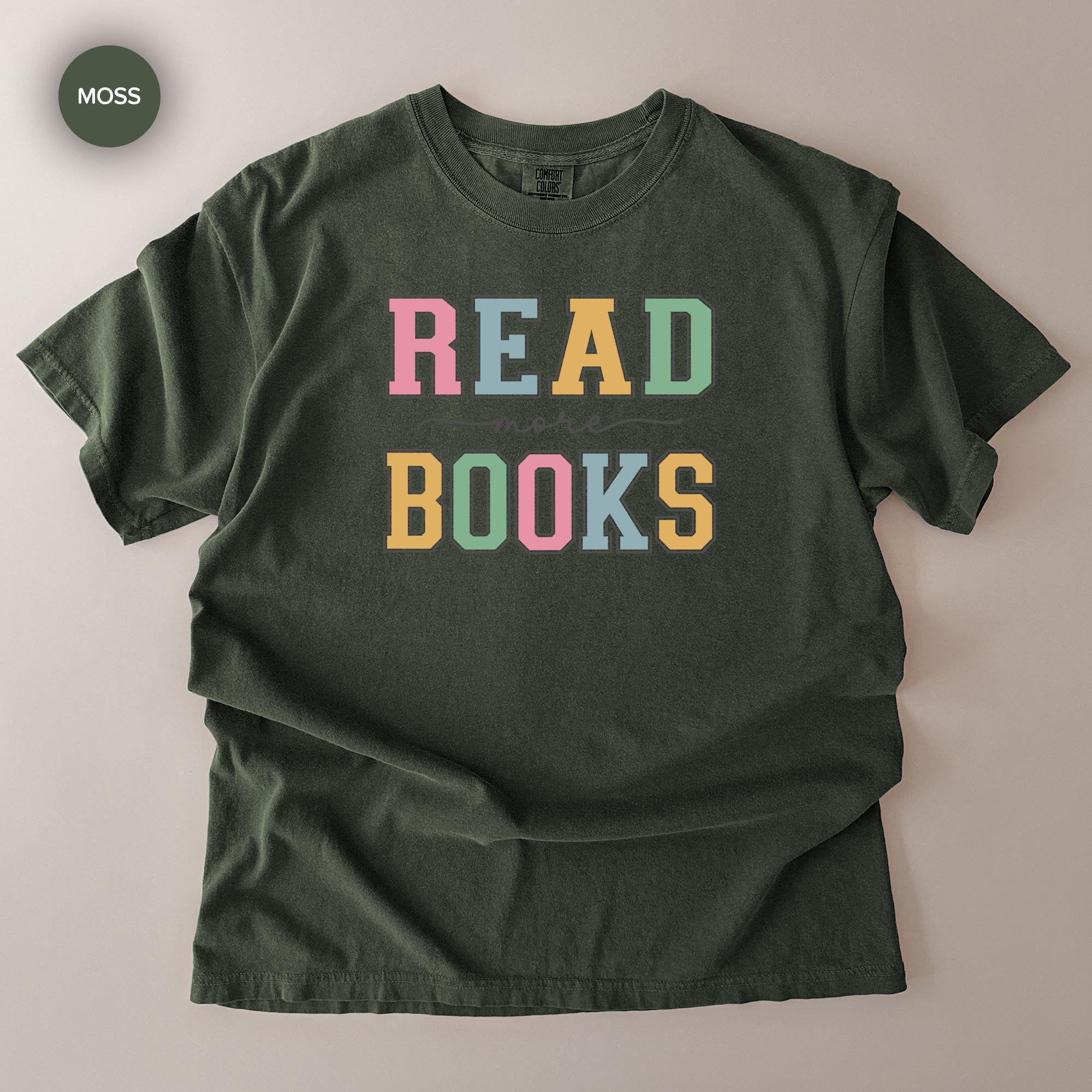 A dark green t-shirt with the text "READ MORE BOOKS" printed on it in a colorful, playful font.
