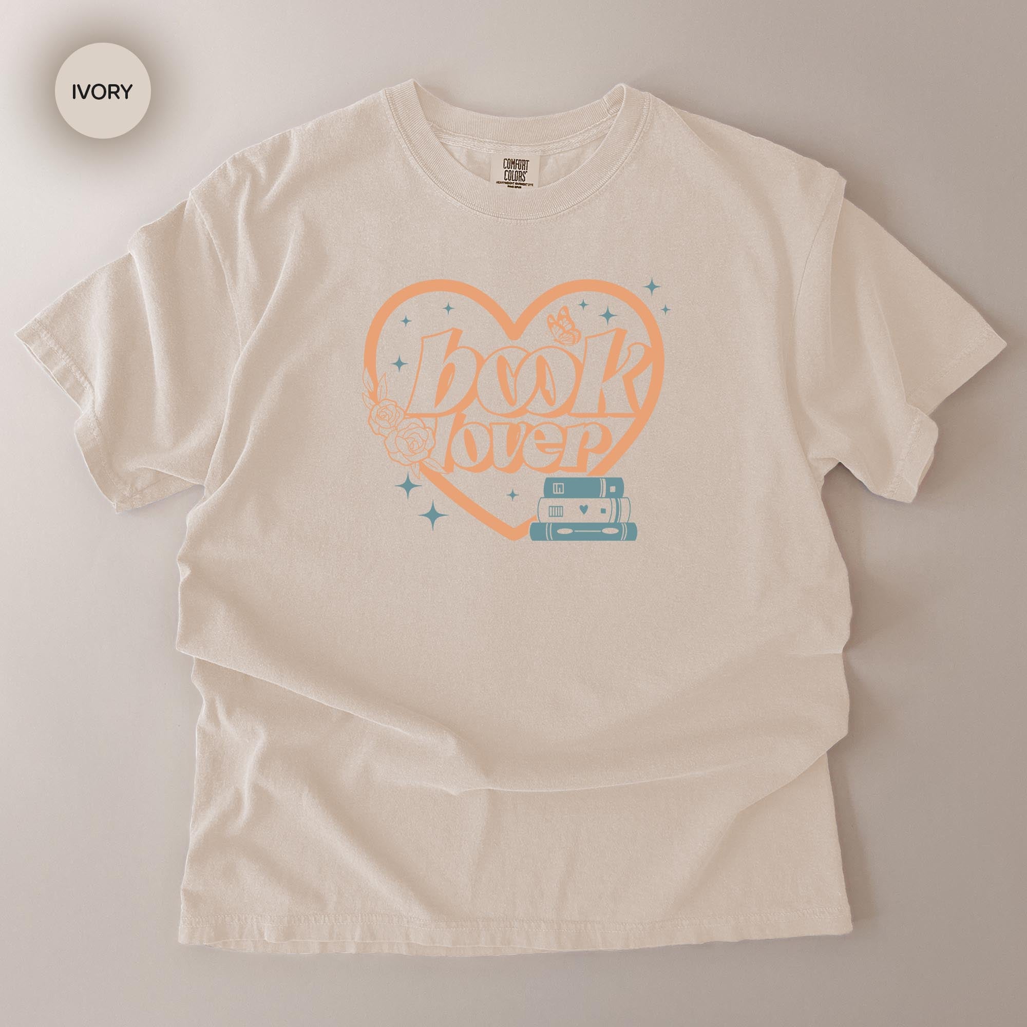 A white t-shirt with a graphic design featuring the text "BOOK LOVER" and a heart-shaped symbol with stars and a book.