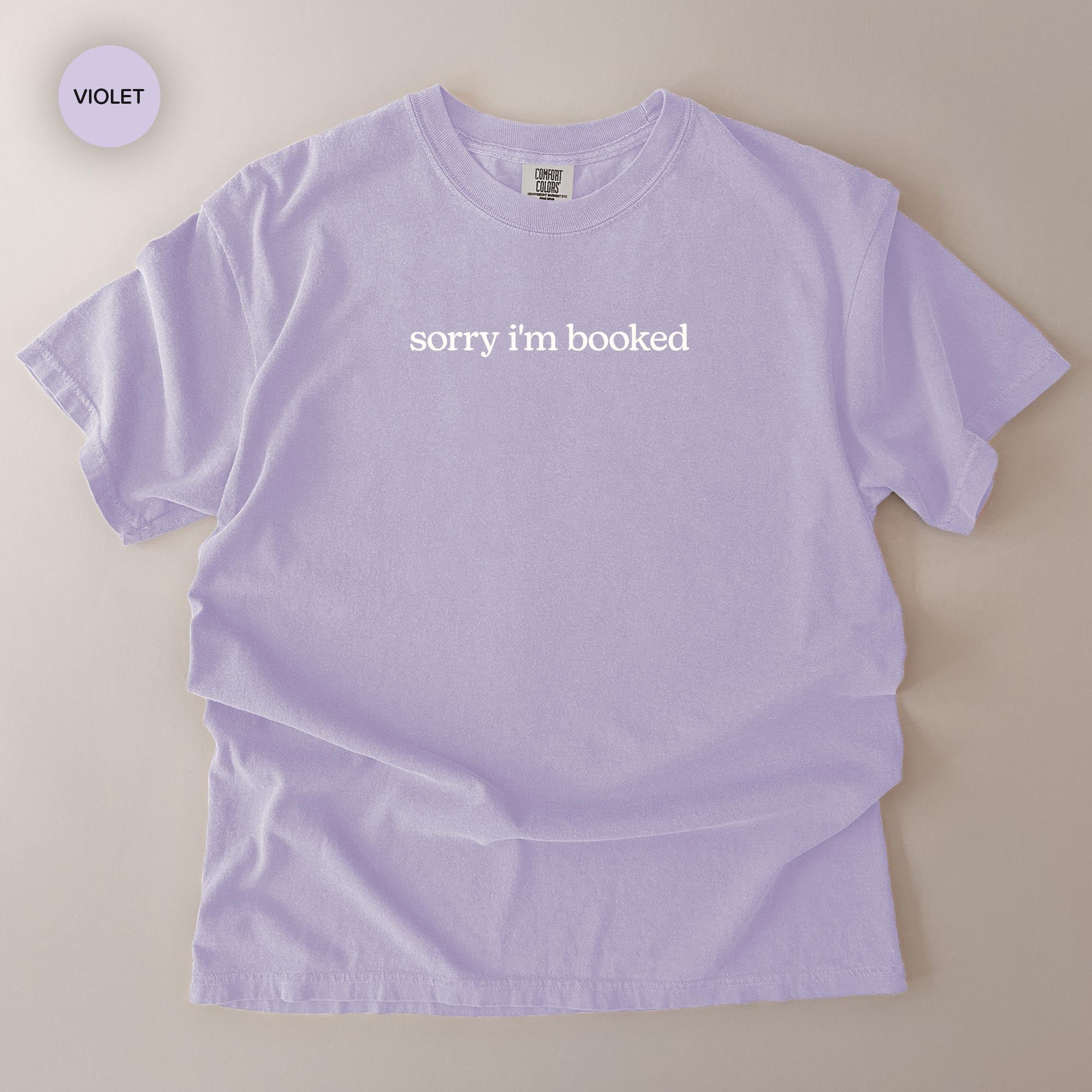 A purple t-shirt with the text "Sorry I'm booked" printed on it.