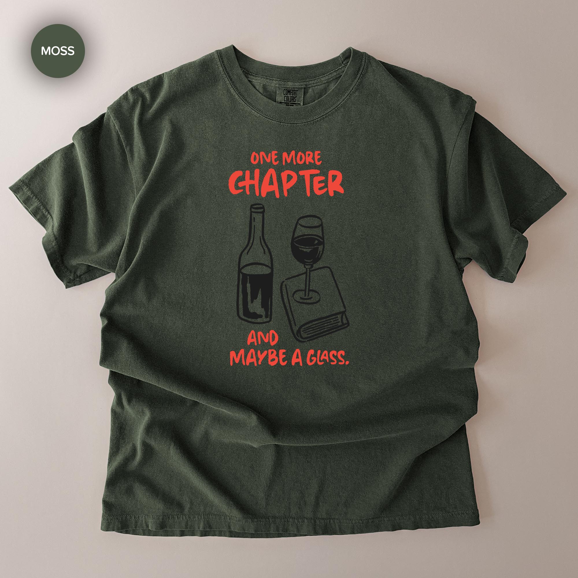 A green t-shirt with a graphic design that says "ONE MORE CHAPTER AND MAYBE A GLASS" along with illustrations of a wine glass and a book.