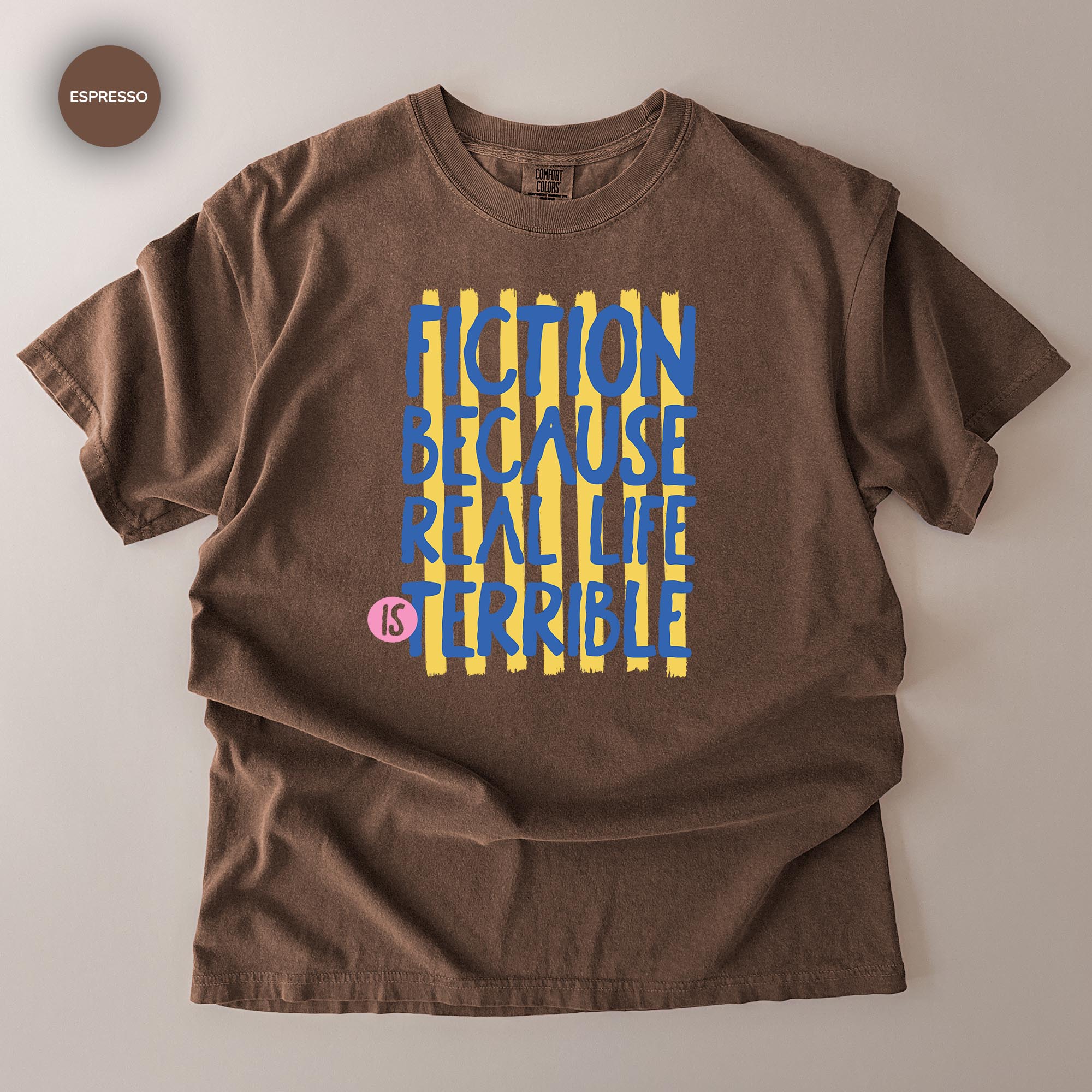 A brown t-shirt with a graphic design featuring the text "FICTION BECAUSE REAL LIFE IS TERRIBLE" in a bold, stylized font.