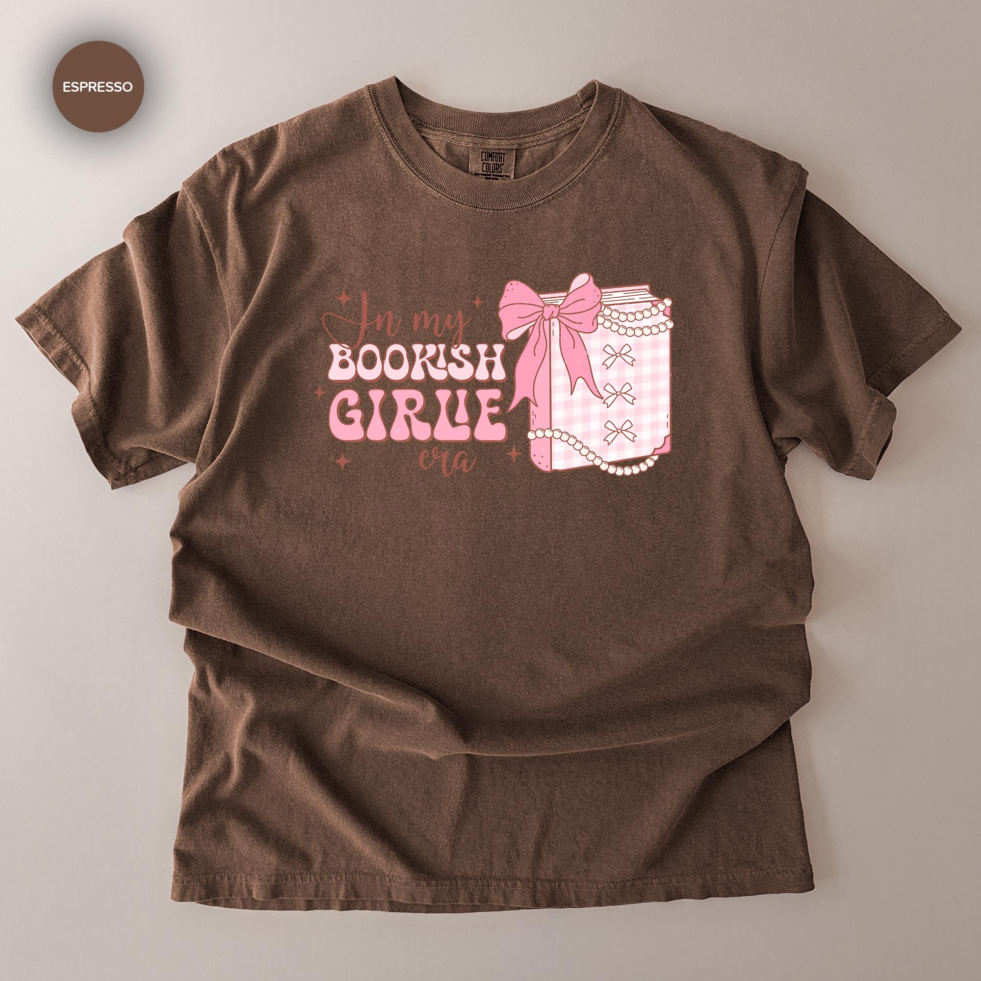 A brown t-shirt with a graphic design that says "In my bookish girl era" and features a bow and a small book.