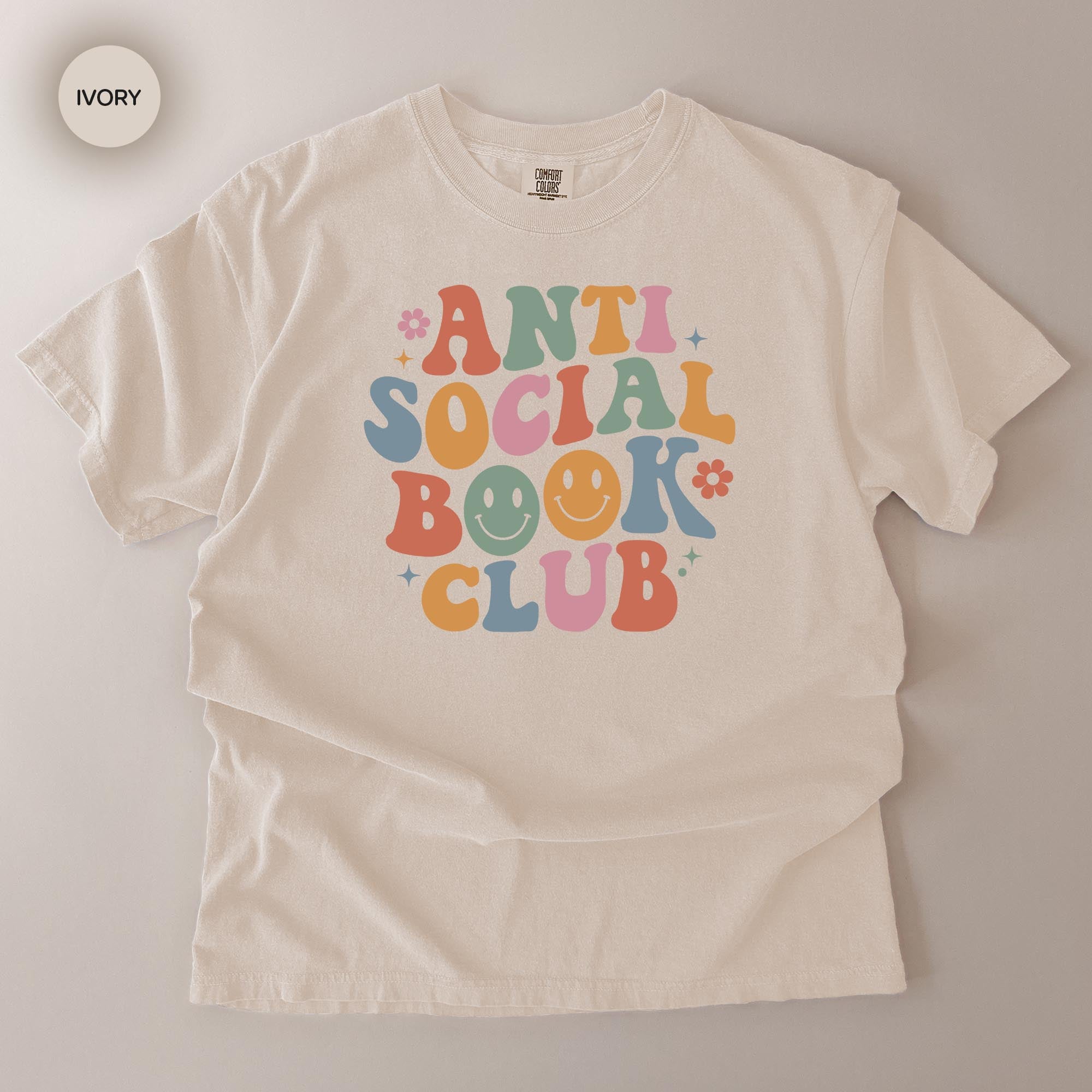 A white t-shirt with a colorful graphic design that says "ANTI SOCIAL BOOK CLUB" in a playful, retro style.