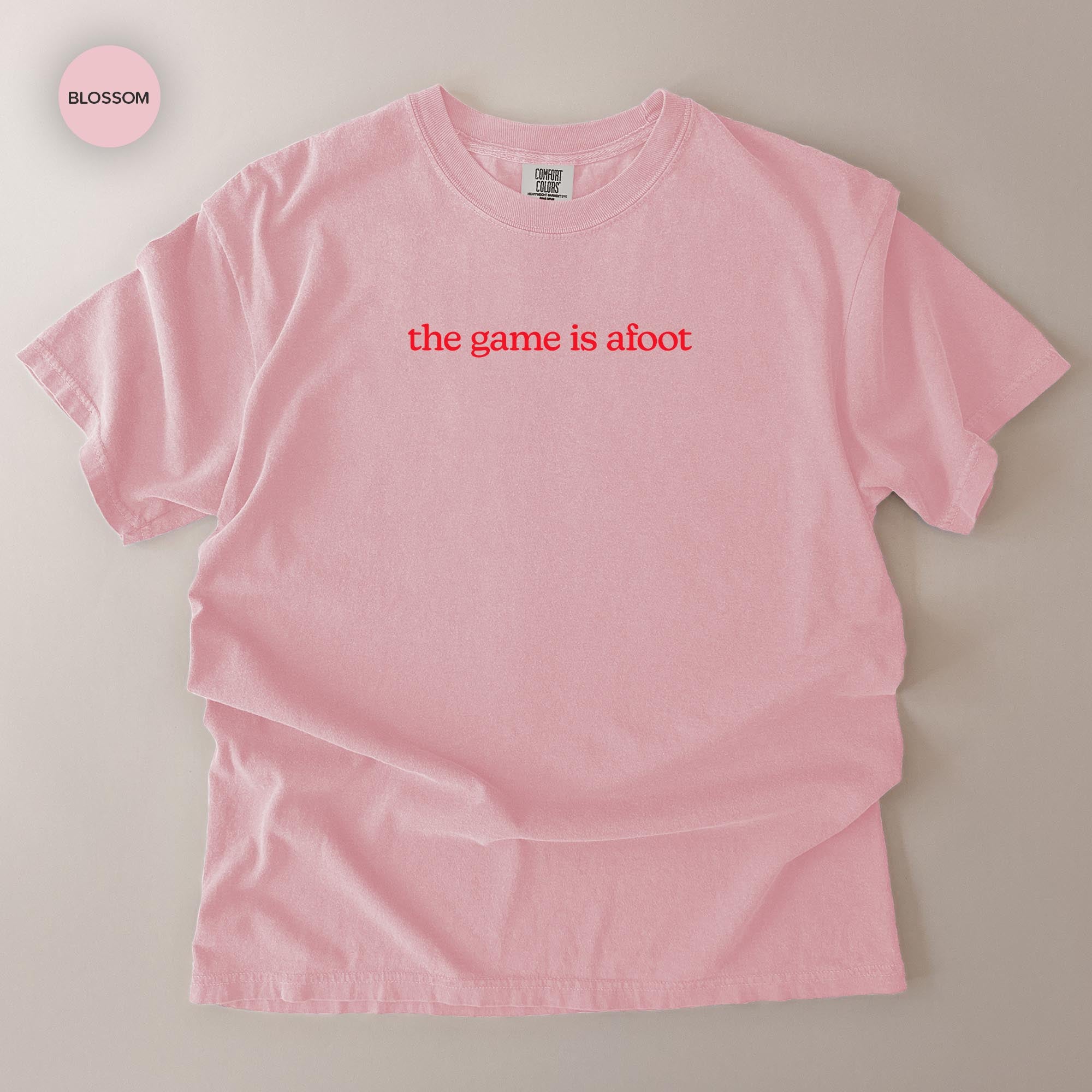 A pink t-shirt with the text "the game is afoot" printed on it.