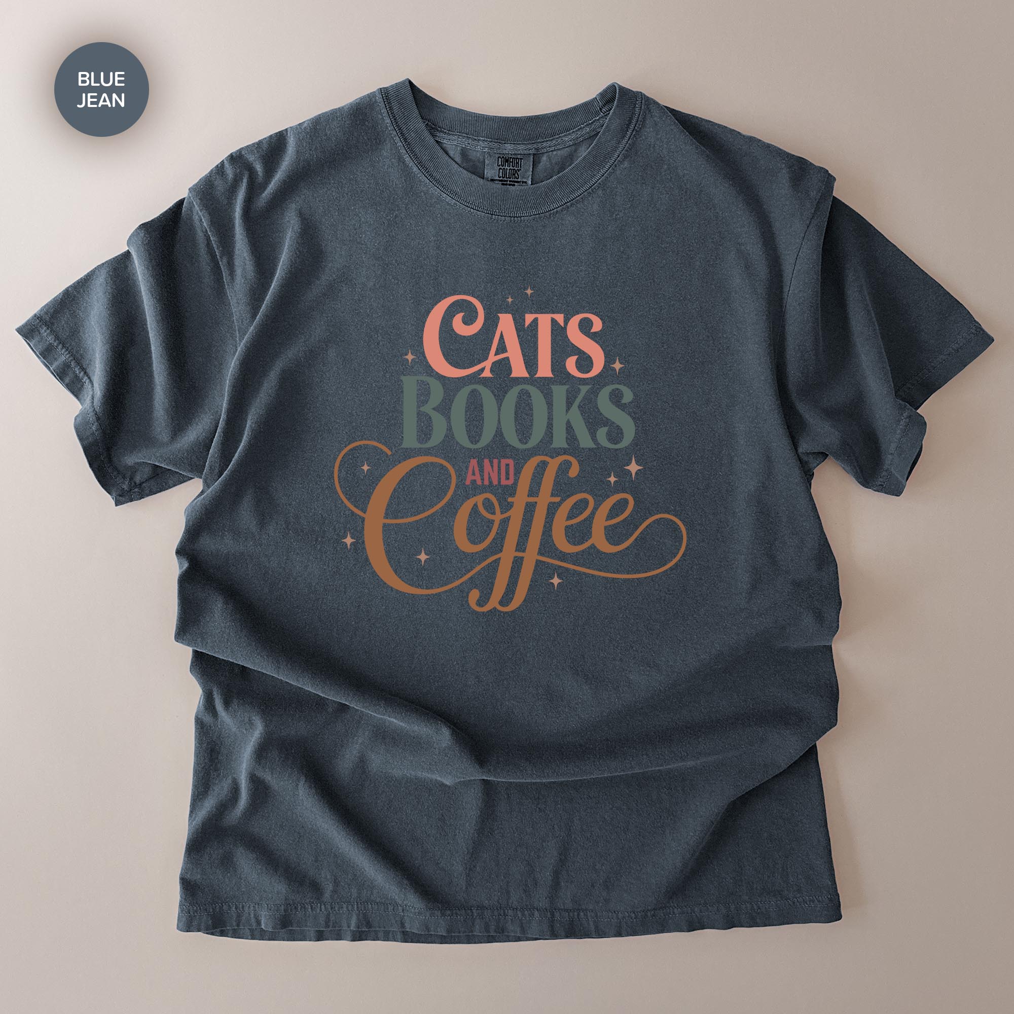 A gray t-shirt with a printed design that says "CATS BOOKS AND COFFEE" in a stylized font.