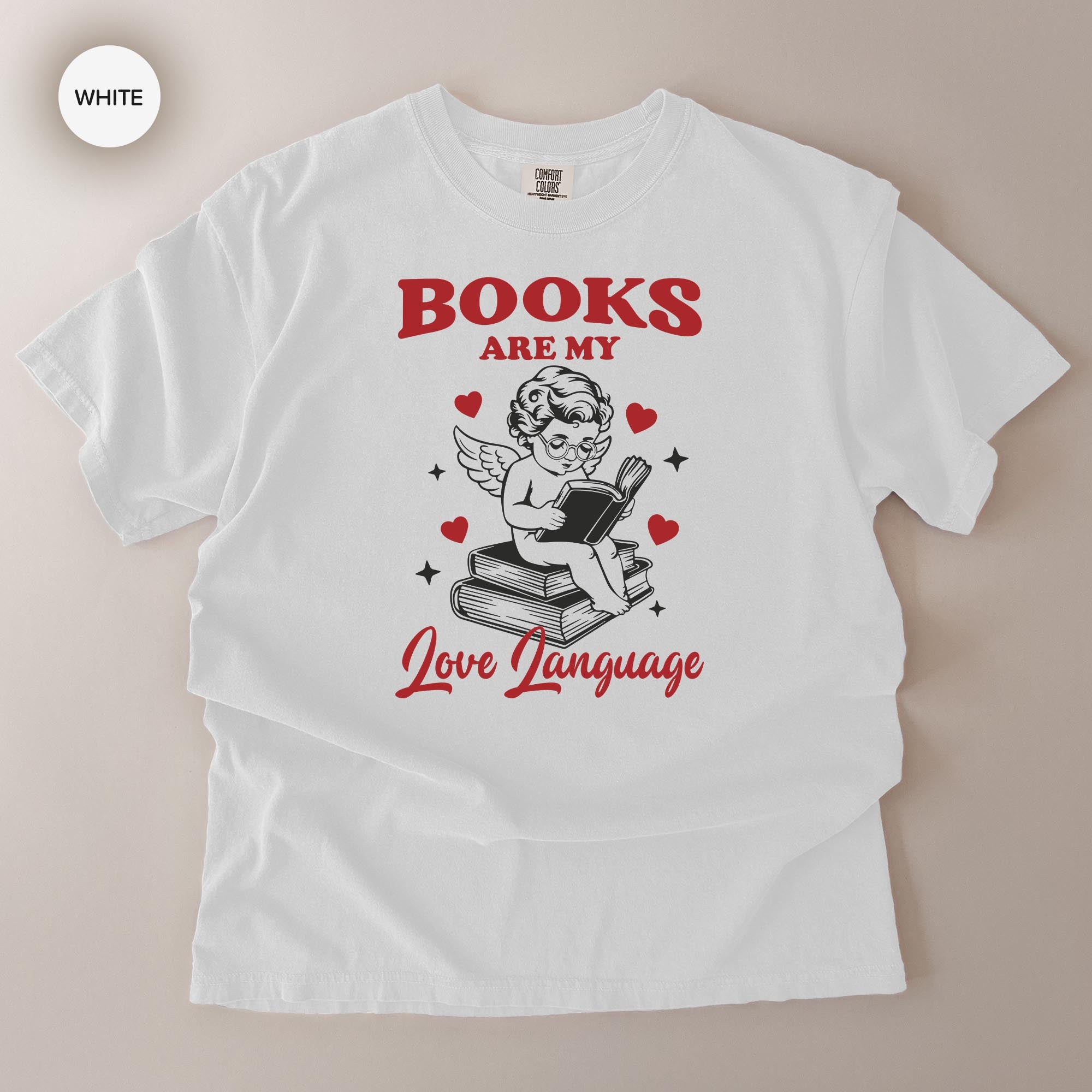 A white t-shirt with a graphic design featuring a cherub holding a book and surrounded by hearts, along with the text "BOOKS ARE MY LOVE LANGUAGE".