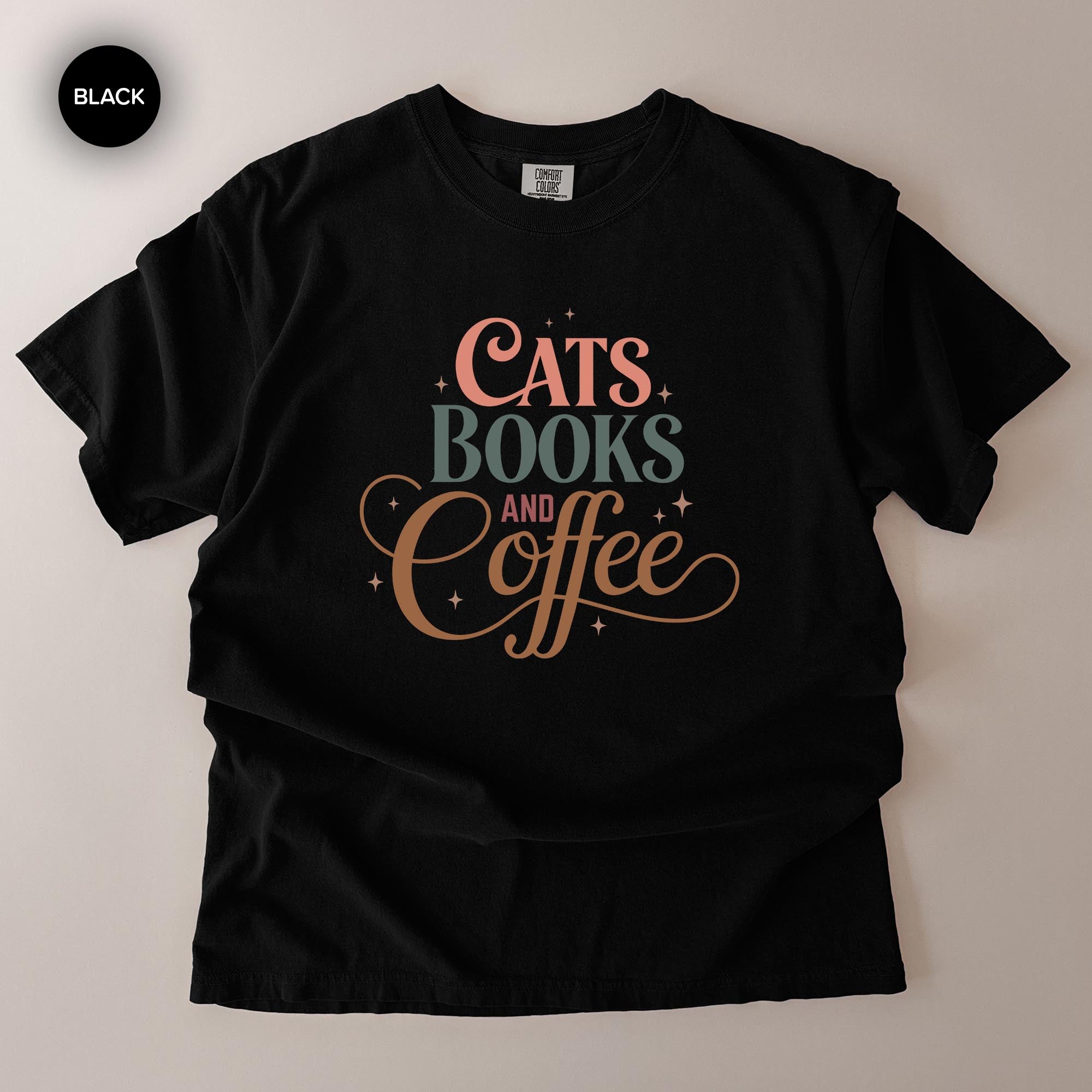 A black t-shirt with a printed design that says "CATS BOOKS AND COFFEE" in a stylized font.