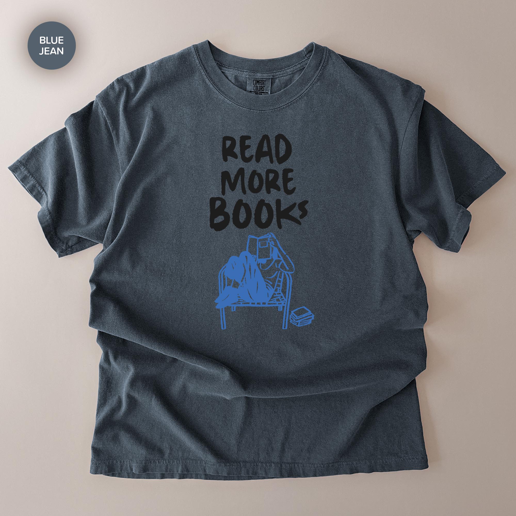 A gray t-shirt with a graphic design that says "READ MORE BOOKS" and features a blue illustration of a person reading a book.