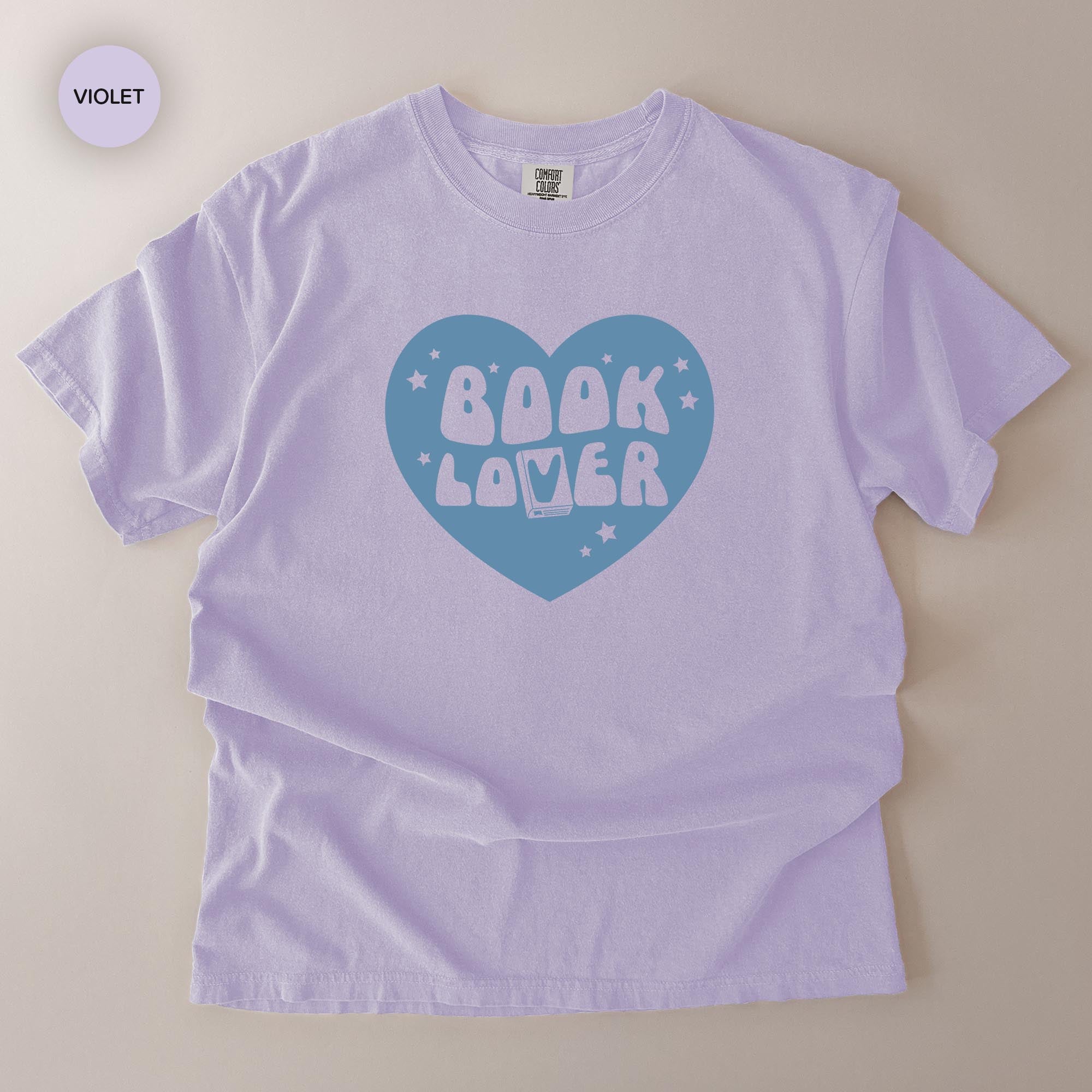 A white t-shirt with a graphic design featuring the text "BOOK LOVER" in a stylized font, surrounded by a heart shape and stars.
