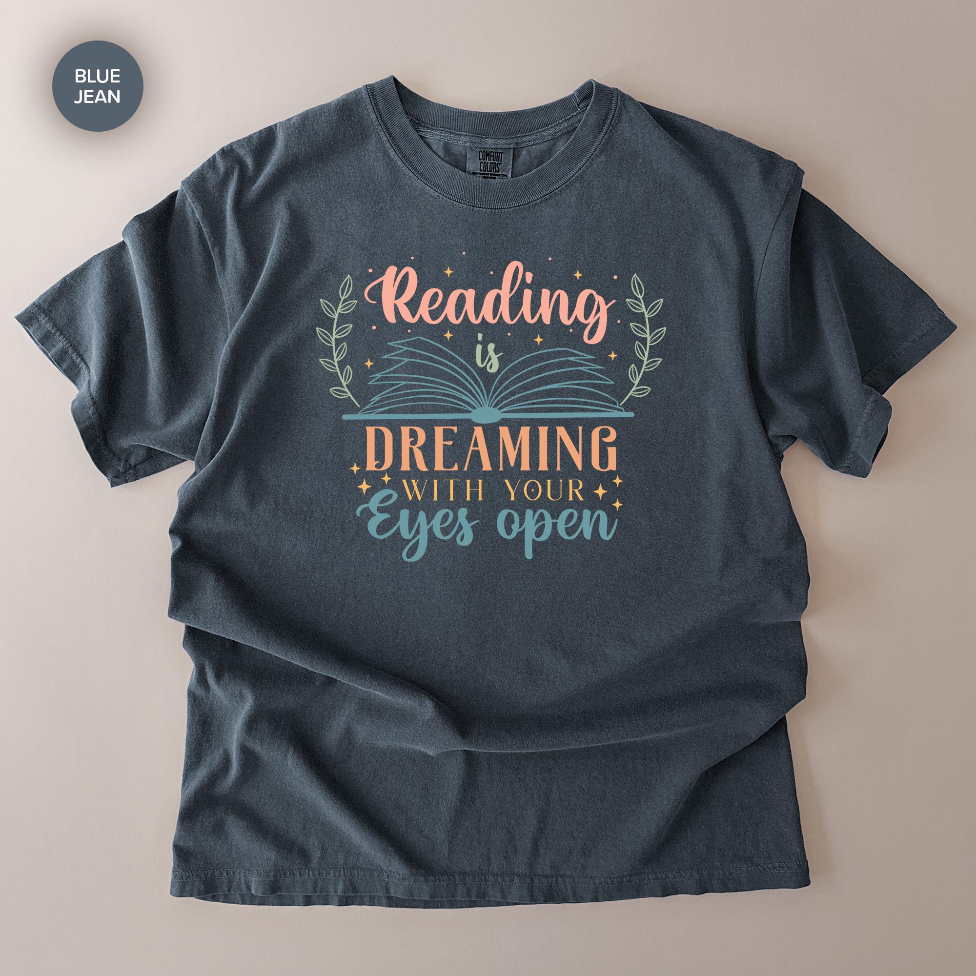 A gray t-shirt with a printed design that says "Reading is Dreaming with your eyes open" in a stylized font.