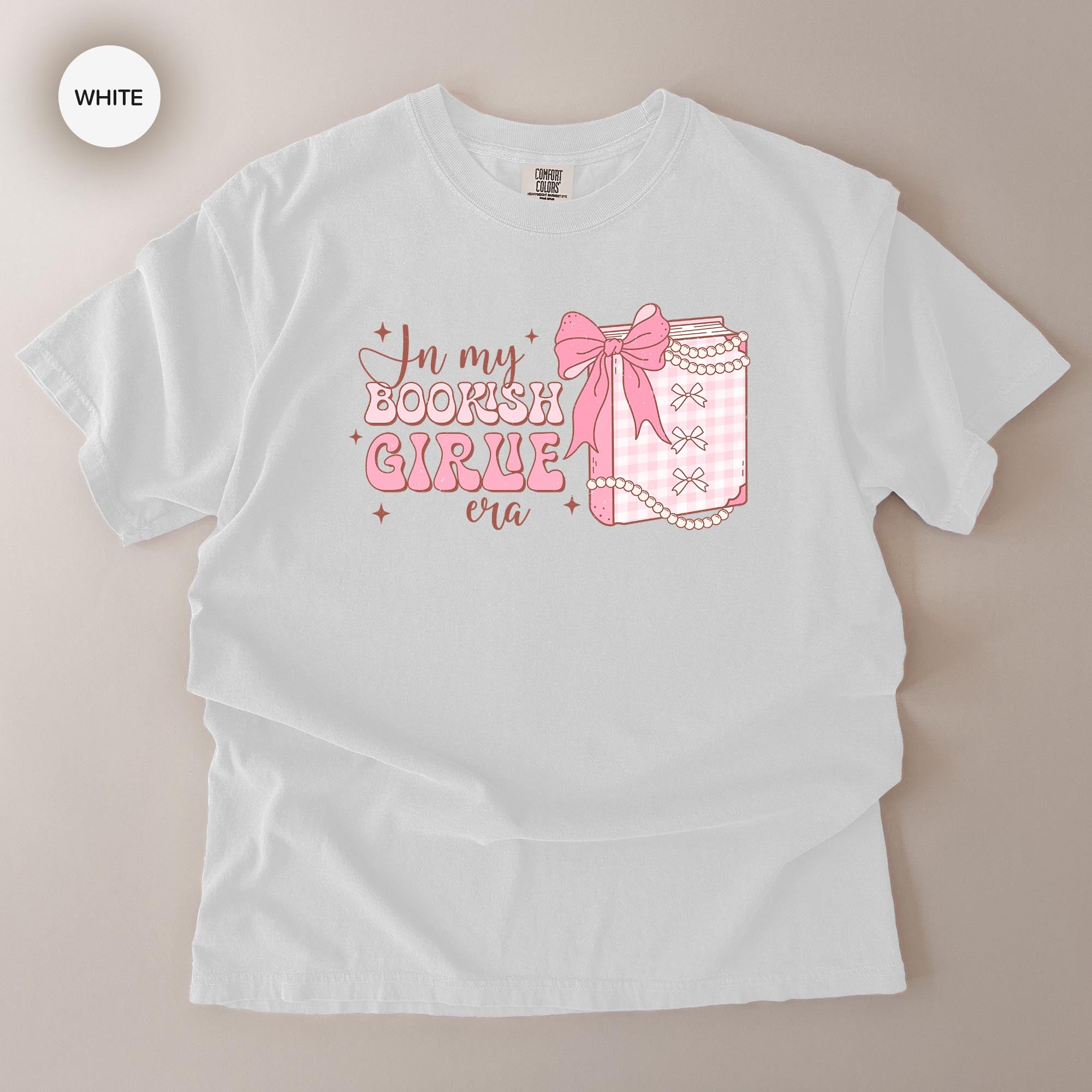 A white t-shirt with a graphic design featuring a bow and text that reads "In my BOOKISH GIRL era".