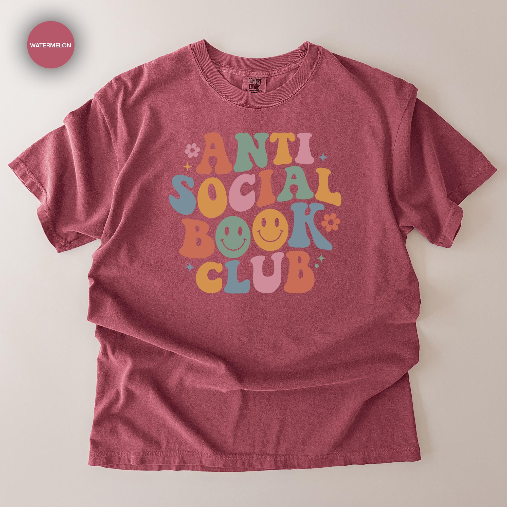 A red t-shirt with a colorful graphic design that says "ANTI SOCIAL BOOK CLUB" in a playful, retro style.