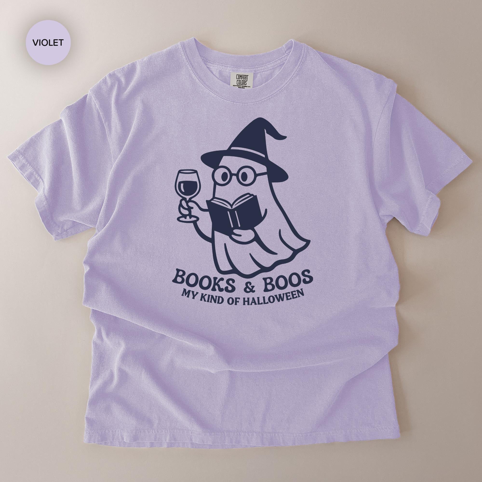 A purple t-shirt with a graphic design depicting a ghost character holding a book and a wine glass, along with the text "Books & Boo's MY KIND OF HALLOWEEN".