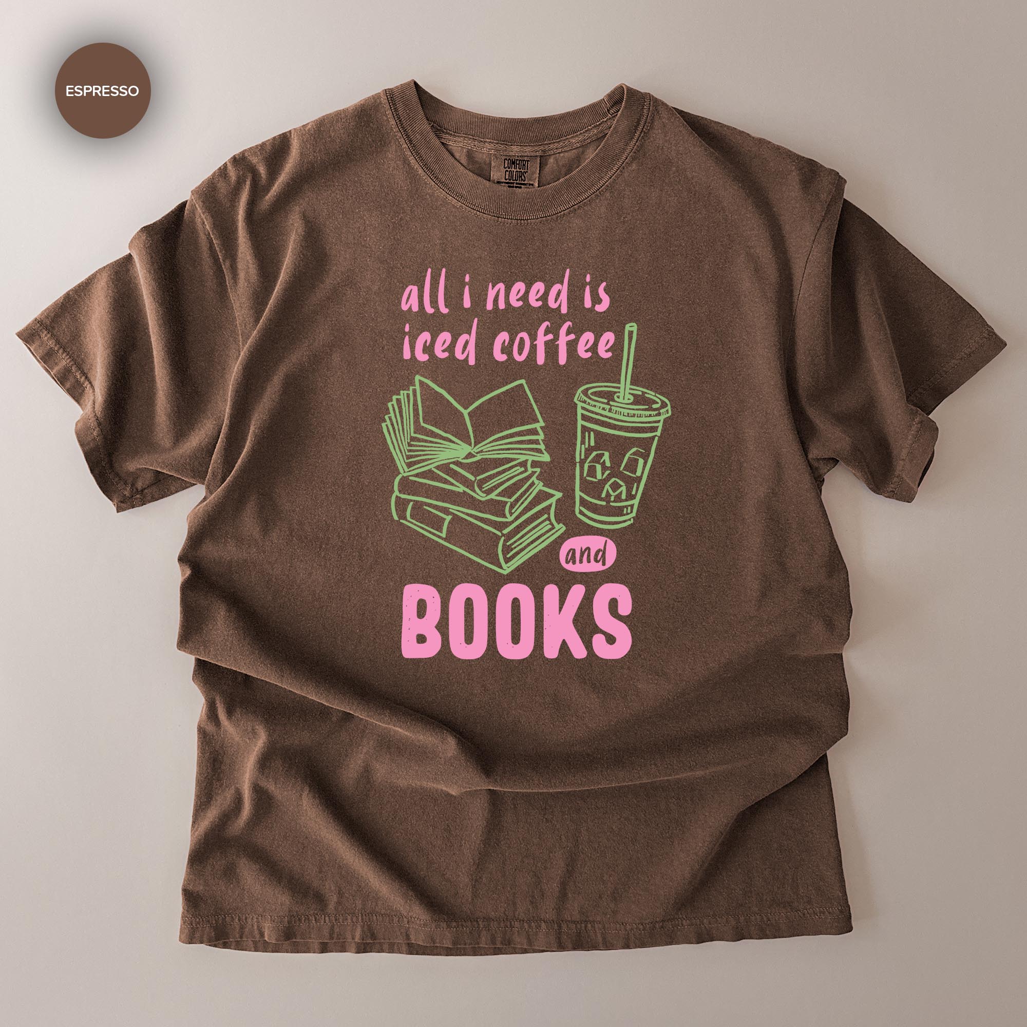 A brown t-shirt with a graphic design that says "all I need is iced coffee and books" in pink and green text.