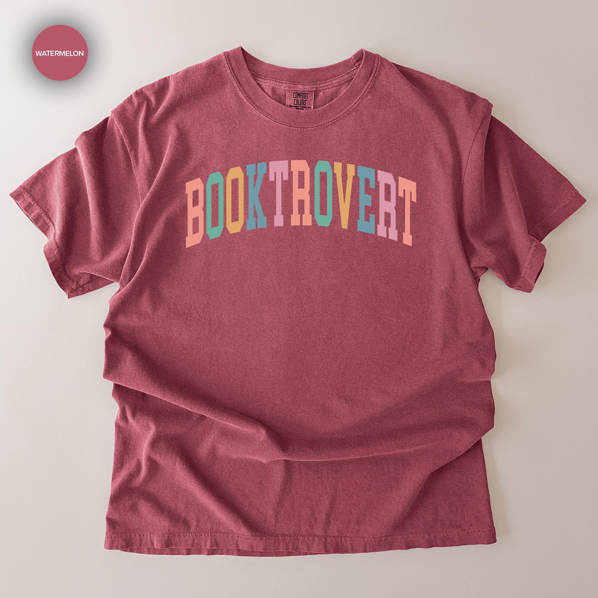 A maroon t-shirt with the text "BOOKTROVERT" printed in a colorful, multicolored font.
