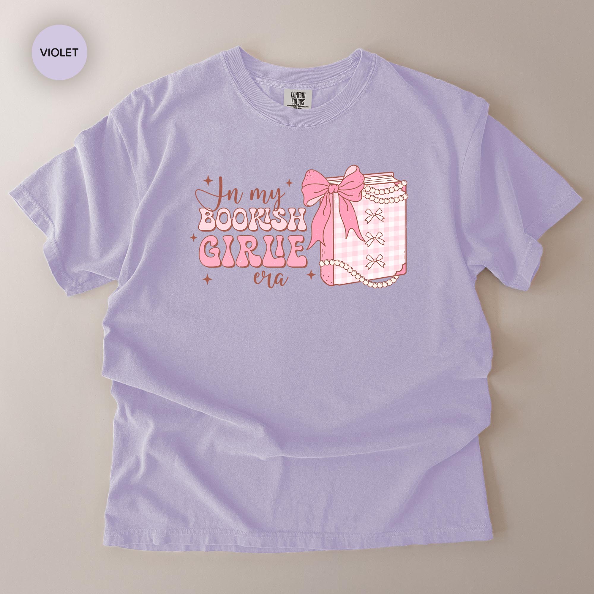 A purple t-shirt with a graphic design featuring a bow and the text "In my BOOKISH GIRL era" printed on it.