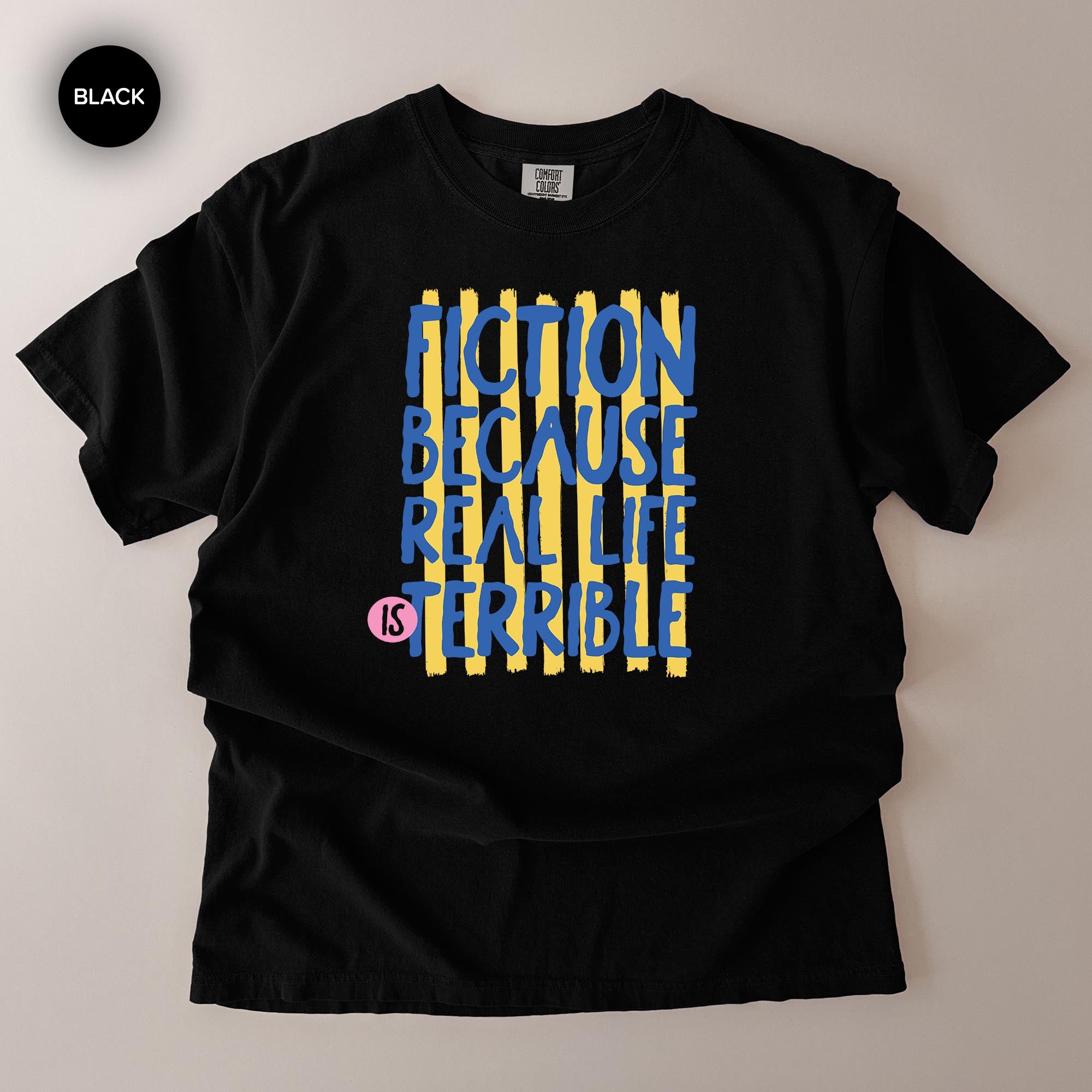 A black t-shirt with a graphic design featuring the text "FICTION BECAUSE REAL LIFE IS TERRIBLE" in blue and yellow colors.