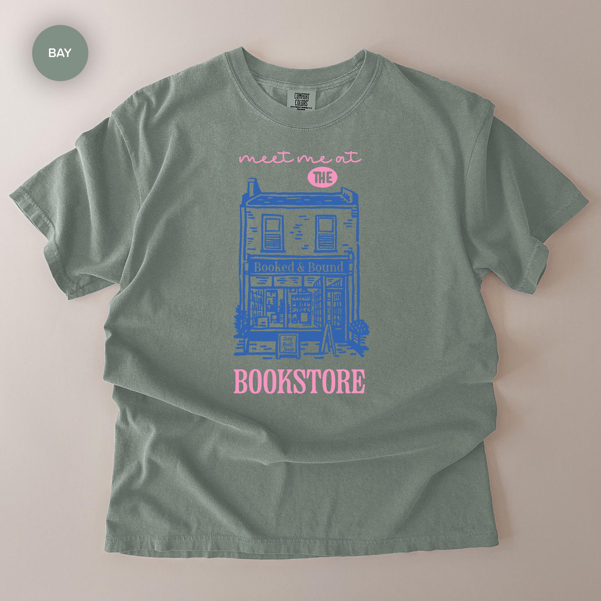 A gray t-shirt with a graphic design depicting a building and the text "Meet me at the BOOKSTORE" printed on it.