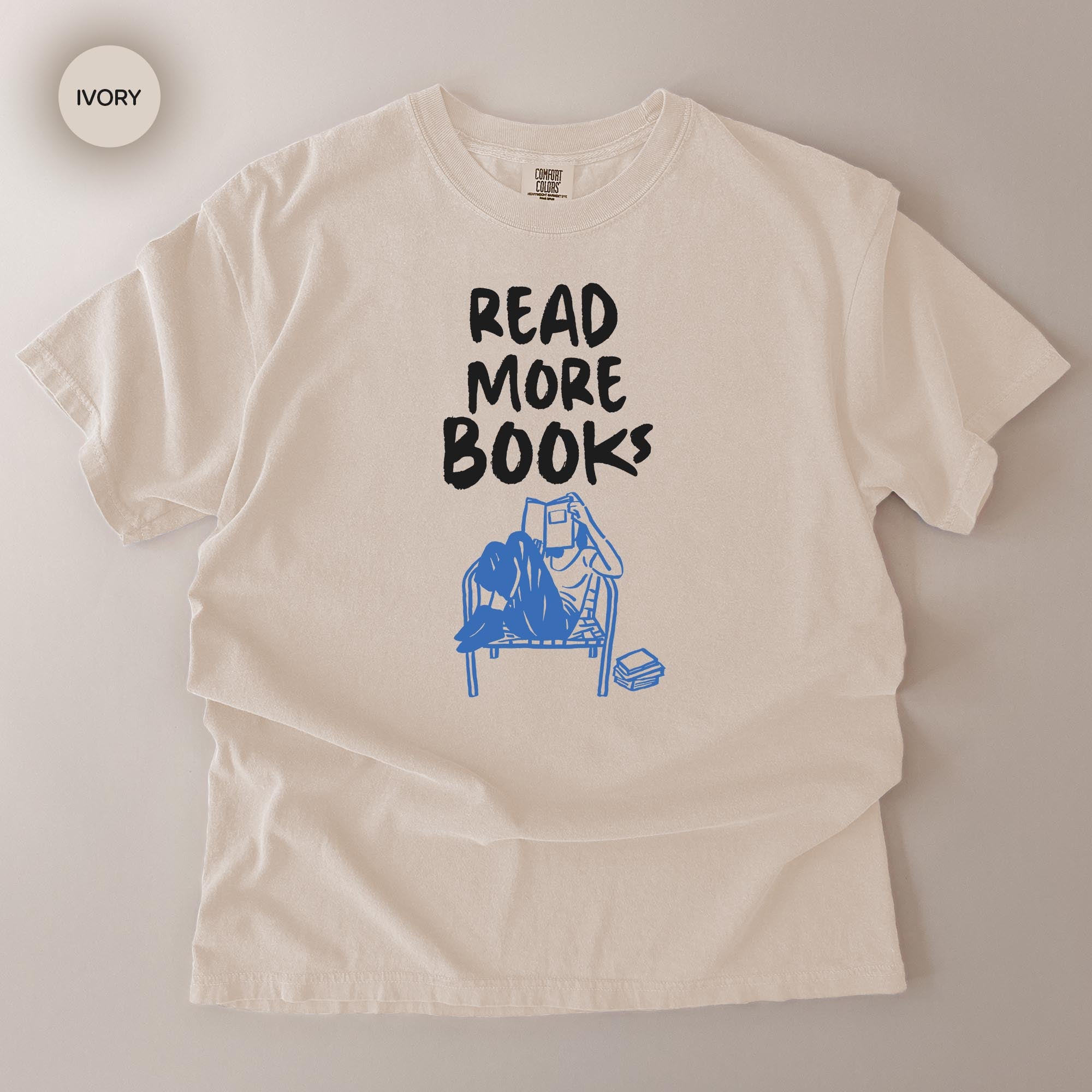 A white t-shirt with the text "READ MORE BOOKS" printed on it, along with a graphic of a person reading a book.