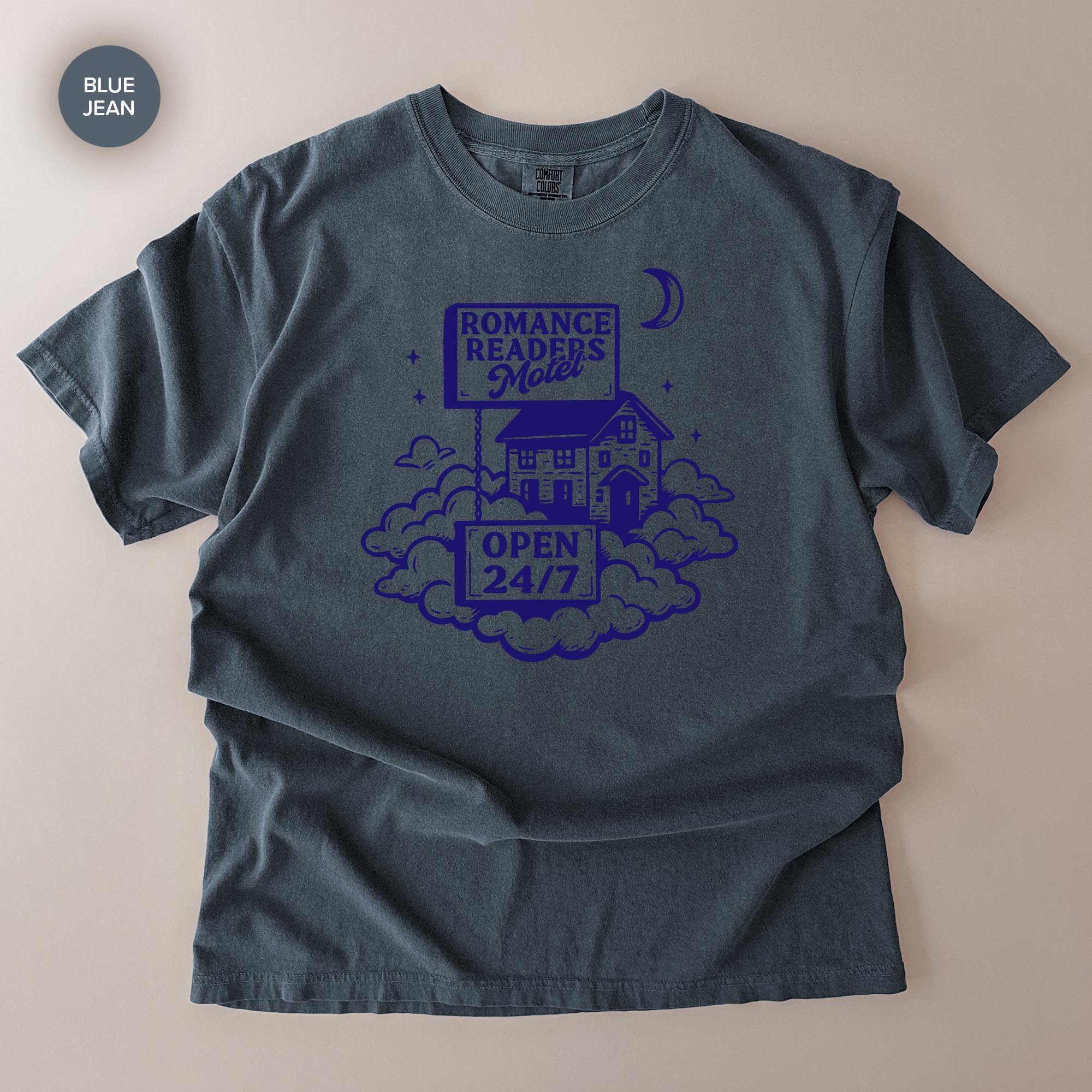 A gray t-shirt with a graphic design featuring a house, clouds, and a crescent moon, along with the text "ROMANCE READERS' ROOM" and "OPEN 24/7".