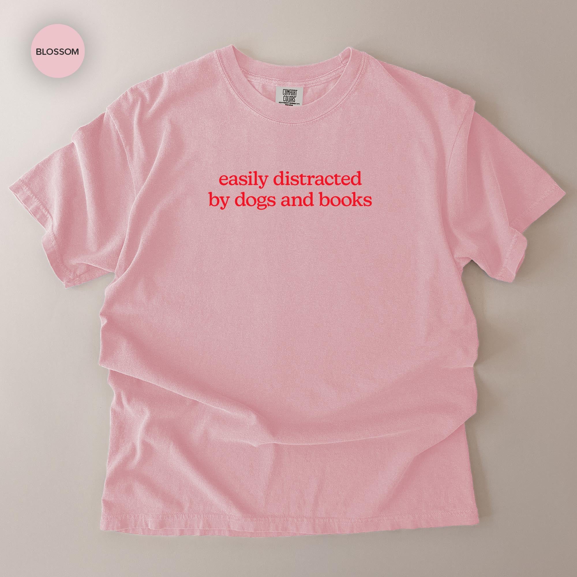 A pink t-shirt with the text "easily distracted by dogs and books" printed on it.