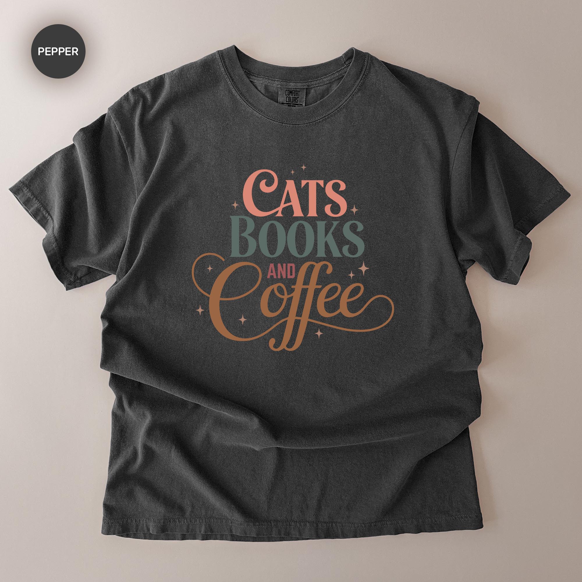A black t-shirt with a printed design that says "CATS BOOKS AND COFFEE" in a stylized font.