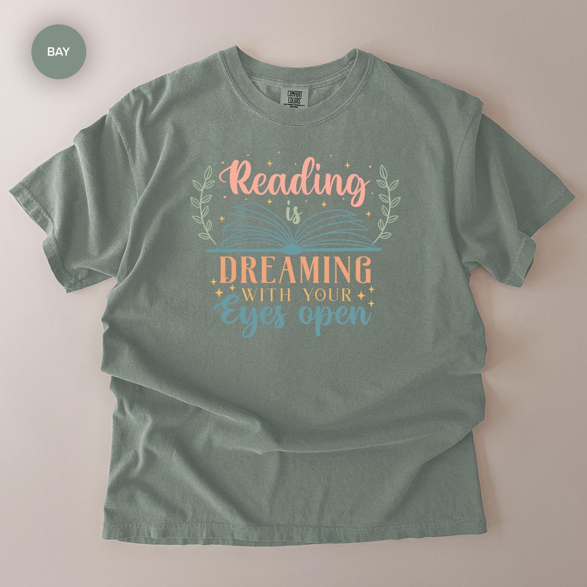 A gray t-shirt with a printed design that says "Reading is Dreaming with your eyes open" in a stylized font.