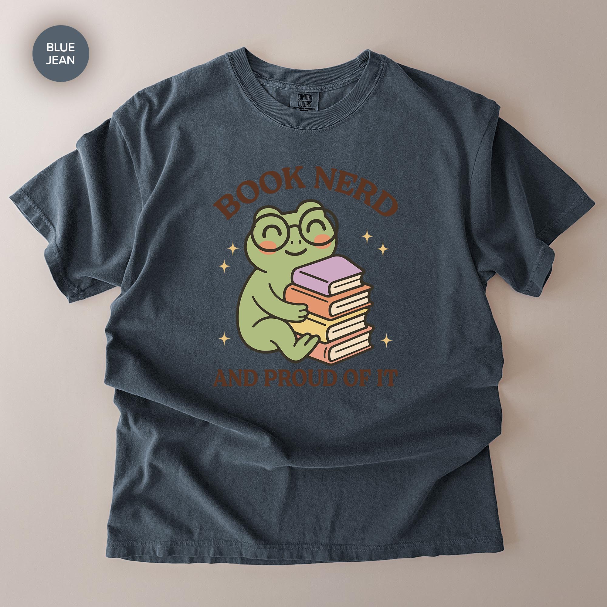 A gray t-shirt with a graphic design featuring a frog wearing glasses and holding a stack of books, along with the text "BOOK NERD AND PROUD OF IT".