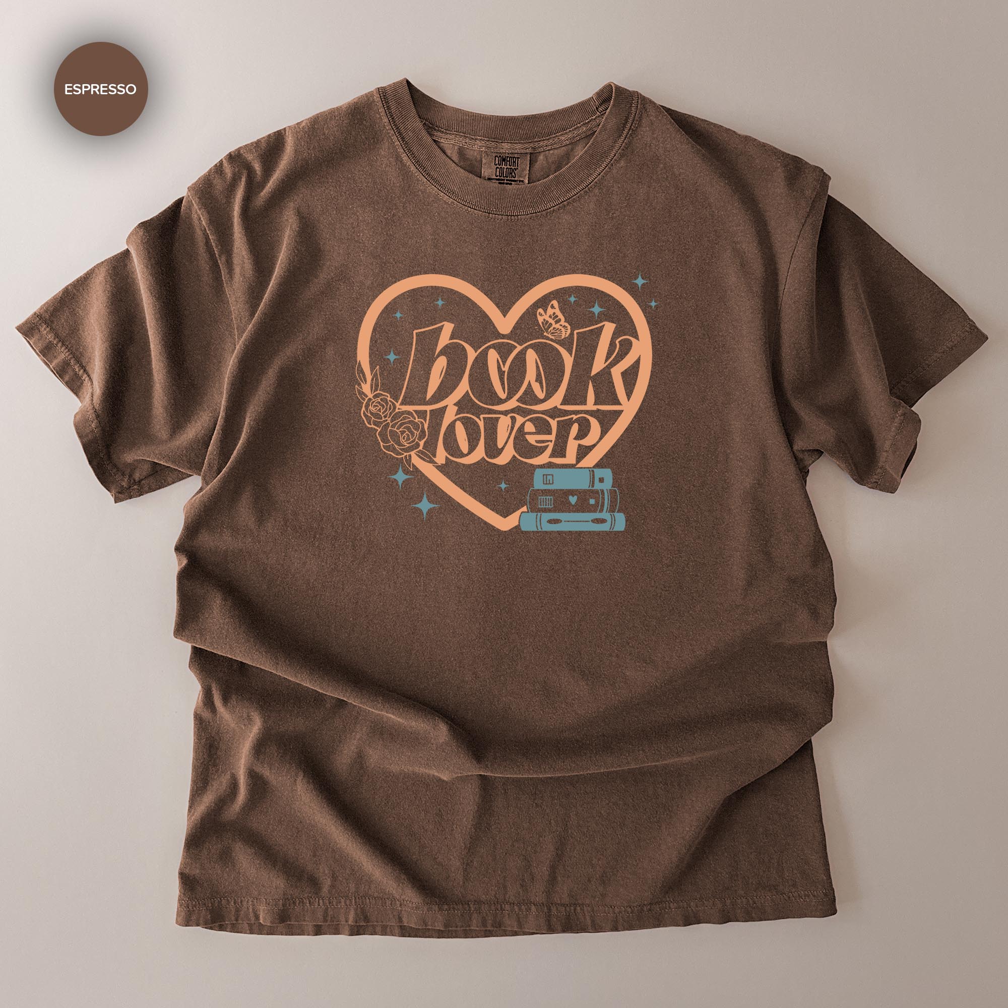 A brown t-shirt with a graphic design featuring the text "book lover" and a heart shape with a camera inside it.