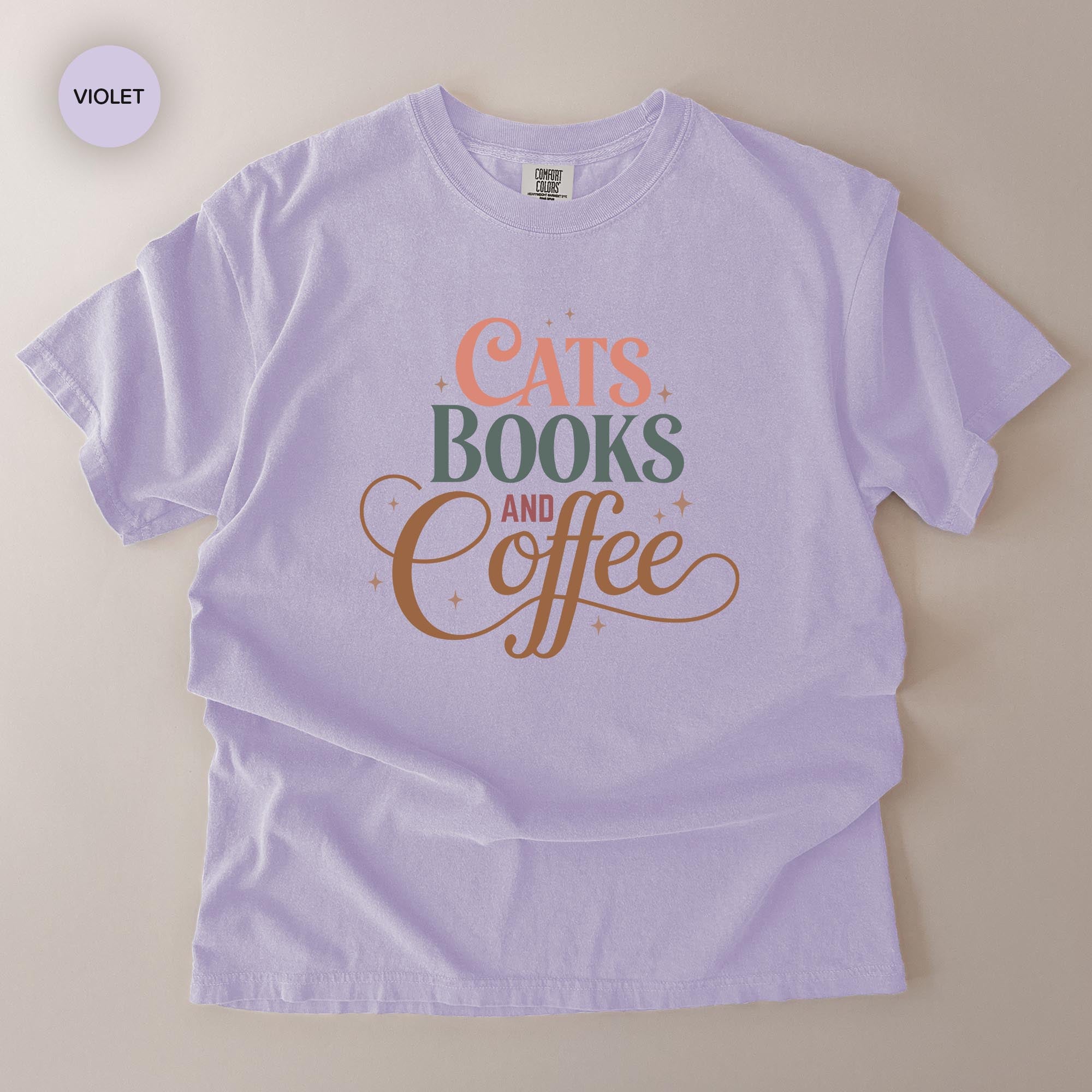 A light purple t-shirt with the text "CATS BOOKS AND COFFEE" printed on it.