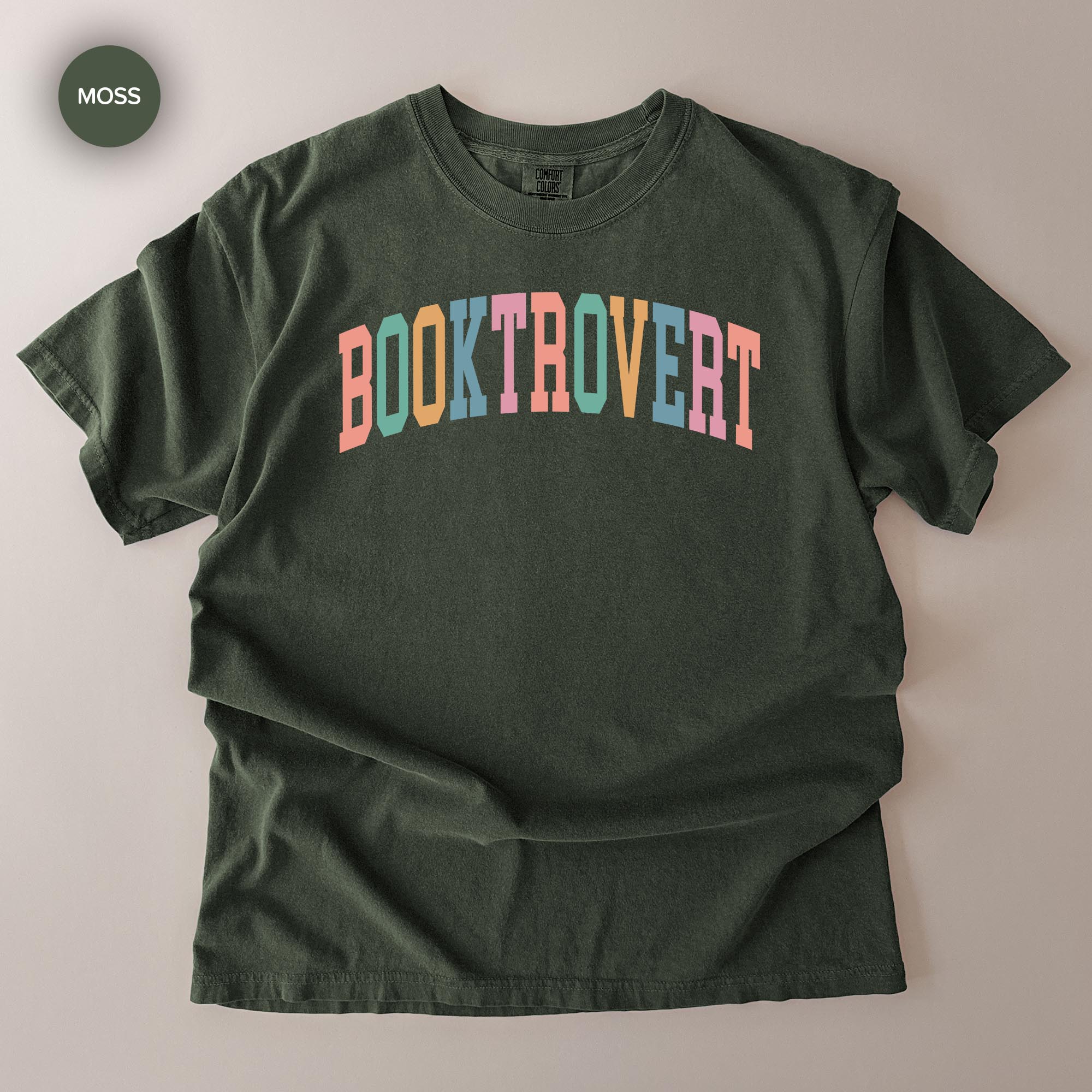 A dark green t-shirt with the text "BOOKTROVERT" printed in a colorful, multicolored font.