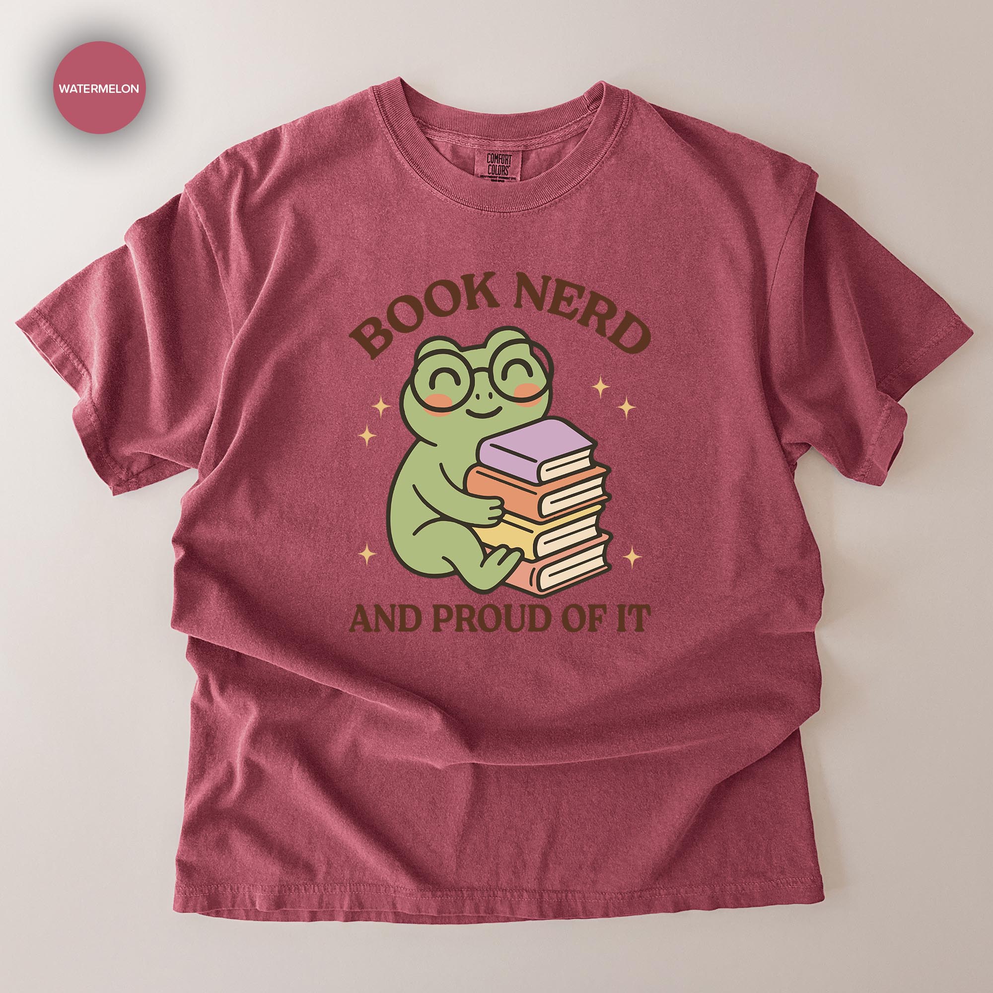 A red t-shirt with a cartoon frog wearing glasses and holding a stack of books, along with the text "BOOK NERD AND PROUD OF IT".