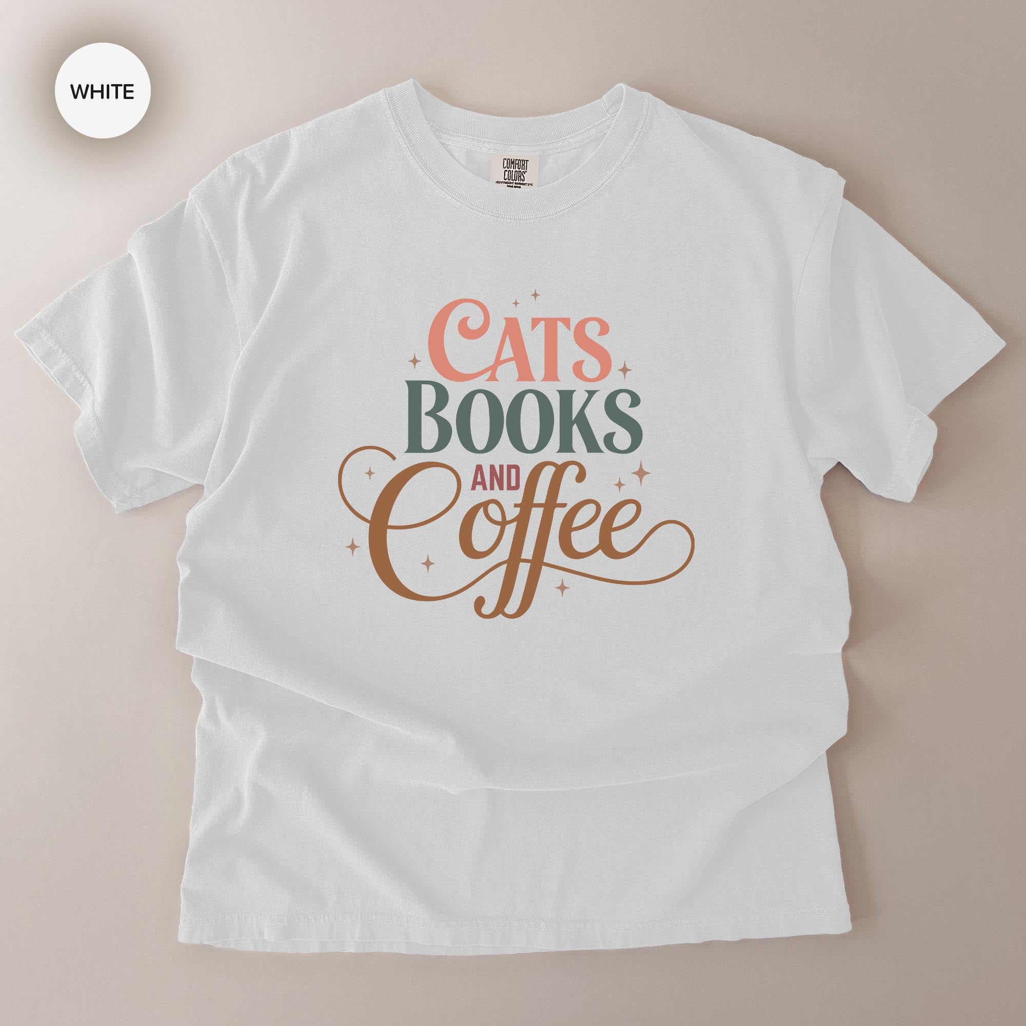 A white t-shirt with a printed design that says "CATS BOOKS AND COFFEE" in a stylized font.