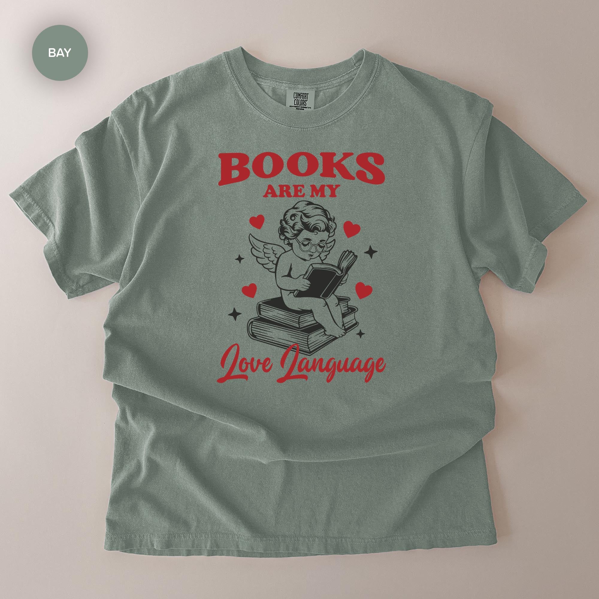A gray t-shirt with a graphic design featuring a cherub holding a book and surrounded by hearts, along with the text "BOOKS ARE MY Love Language".