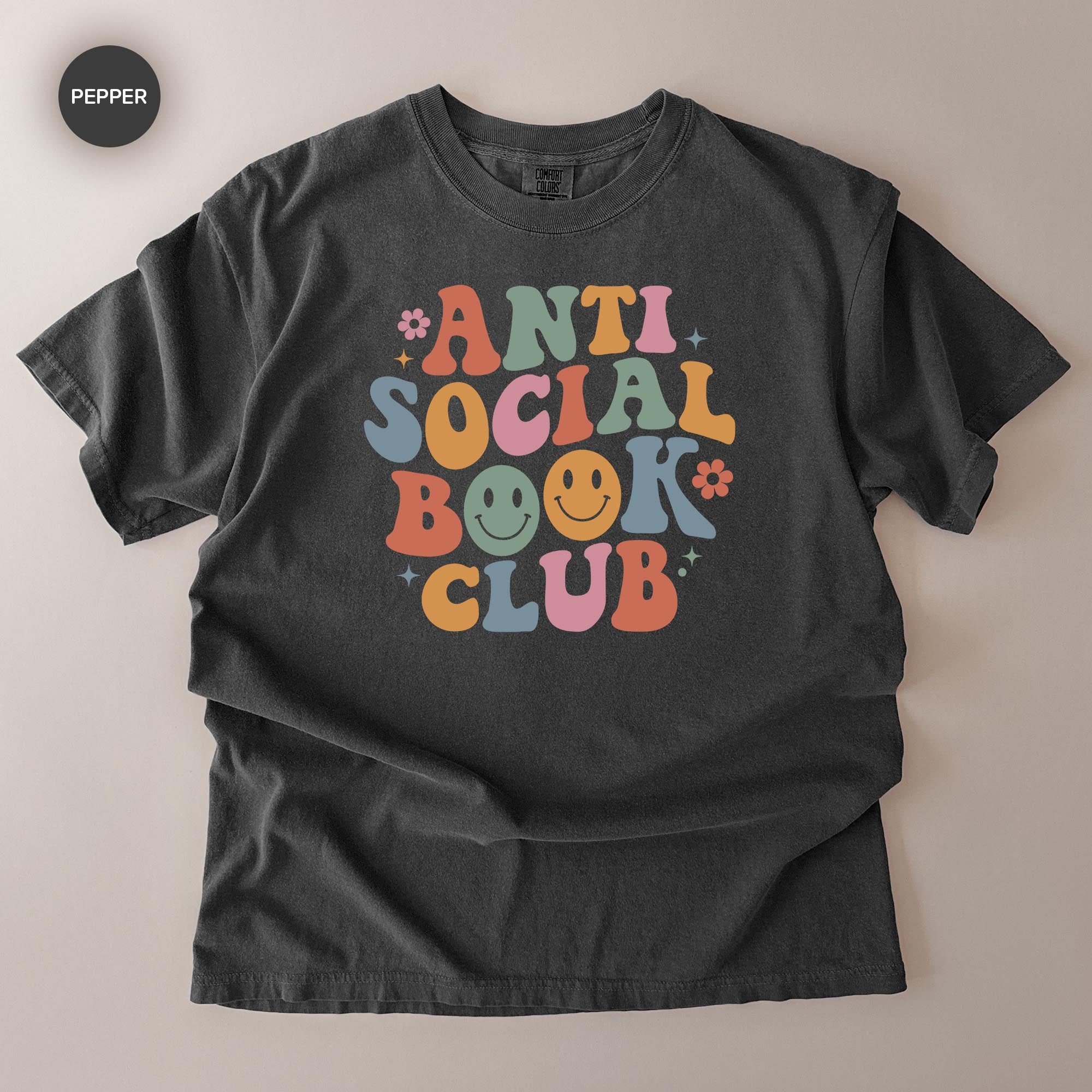 A black t-shirt with a colorful graphic design that says "ANTI SOCIAL BOOK CLUB" in a retro style.