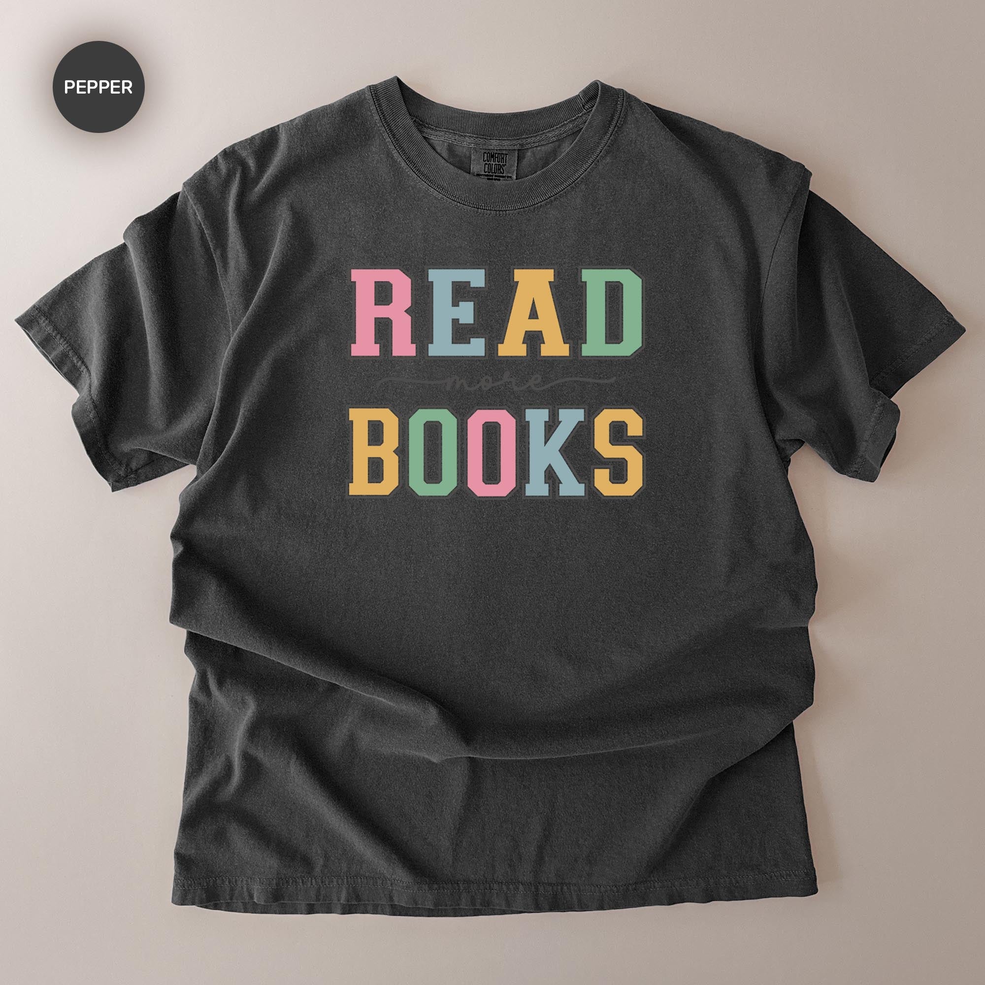 A black t-shirt with the text "READ MORE BOOKS" printed on it in a colorful, playful font.