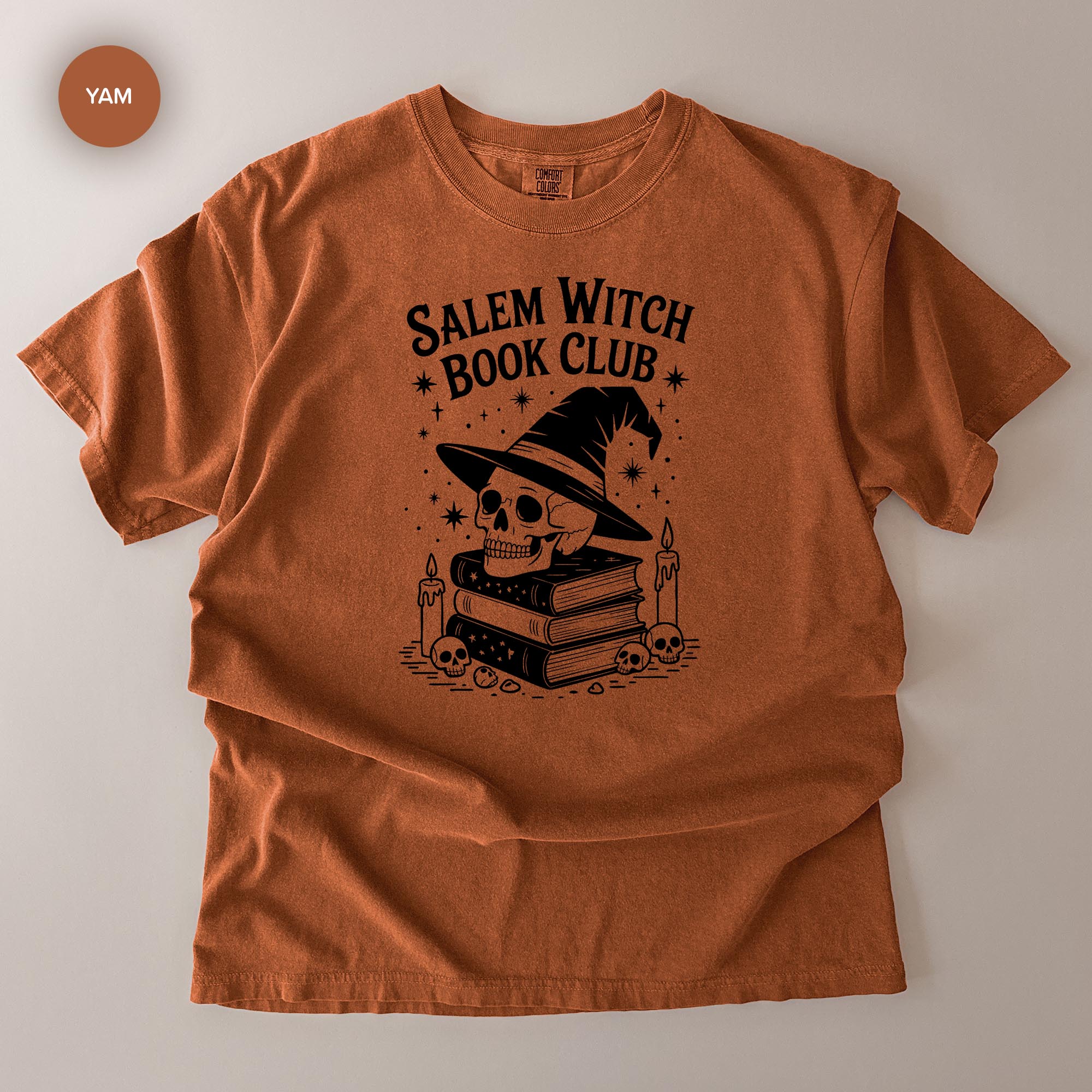 The image is a t-shirt with a graphic design featuring a skull wearing a witch's hat, surrounded by books and candles, with the text "Salem Witch Book Club" printed on it.