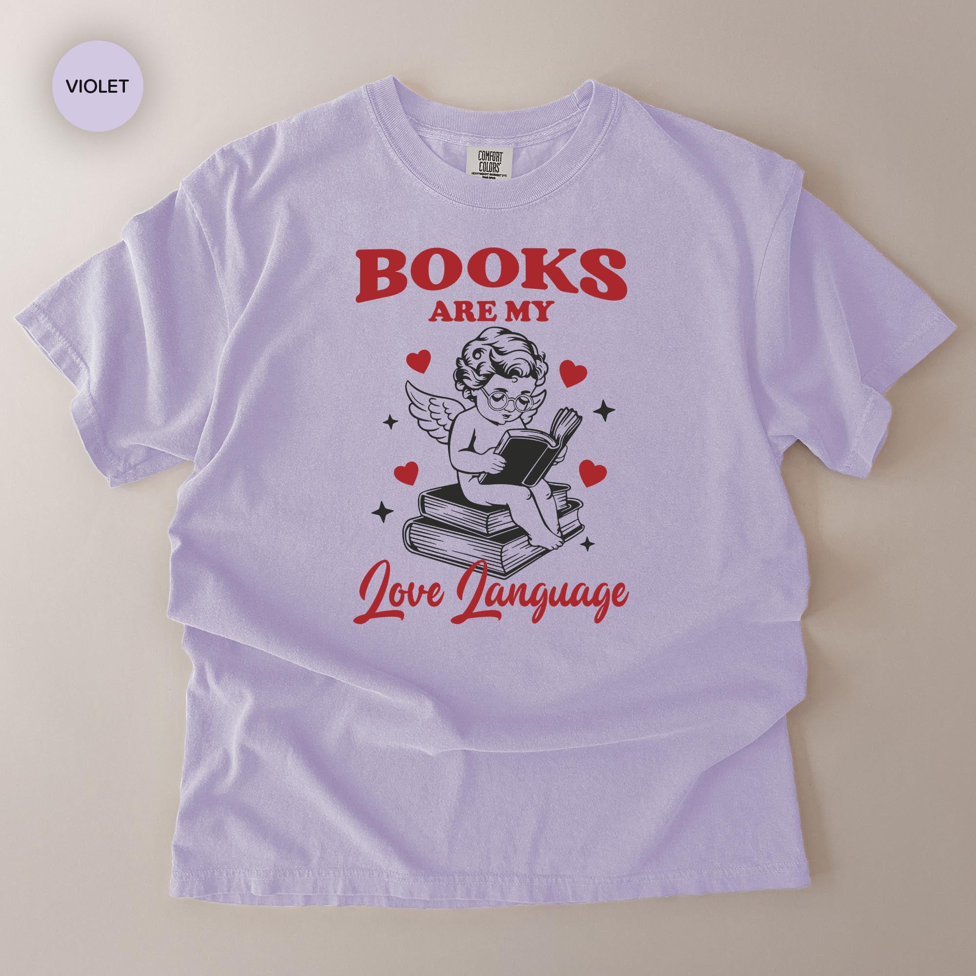 A white t-shirt with a graphic design featuring a cherub holding a book and the text "Books are my love language" along with a heart symbol.