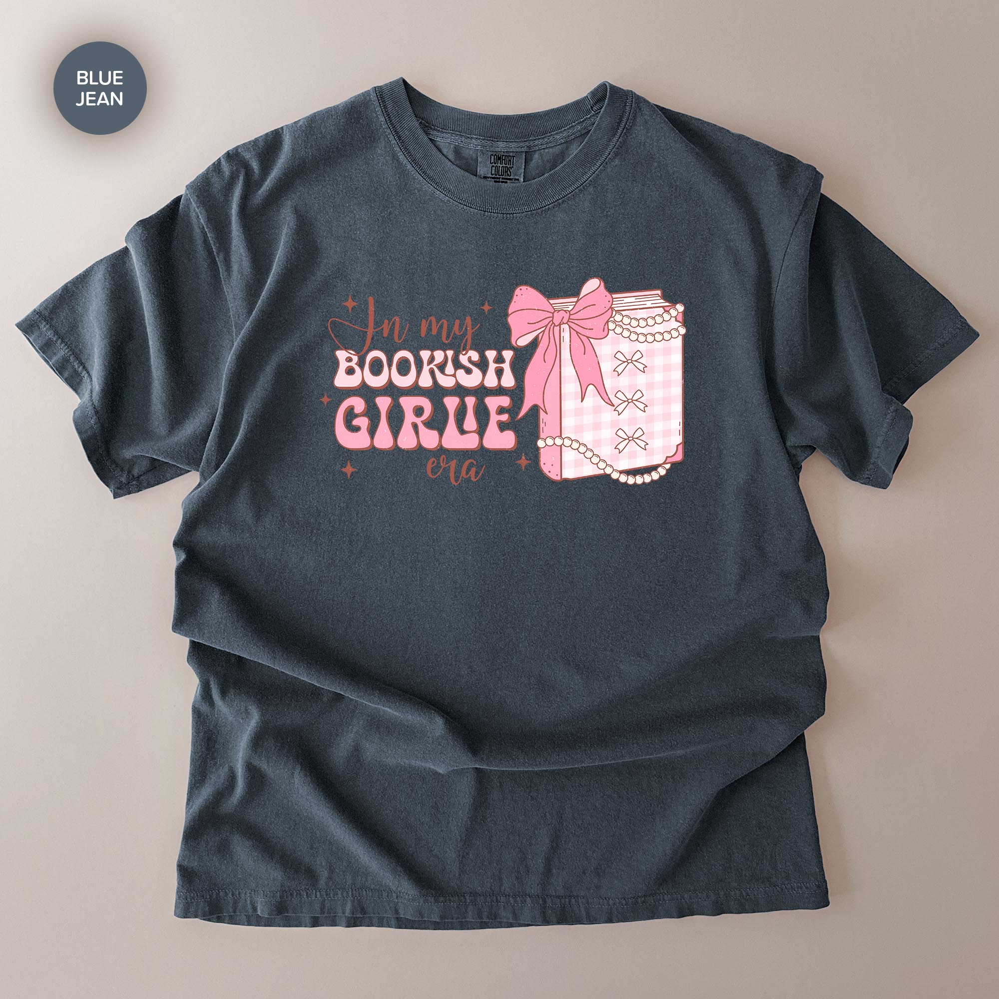 A gray t-shirt with a graphic design featuring a bow and text that says "In my BOOKISH GIRLE era".